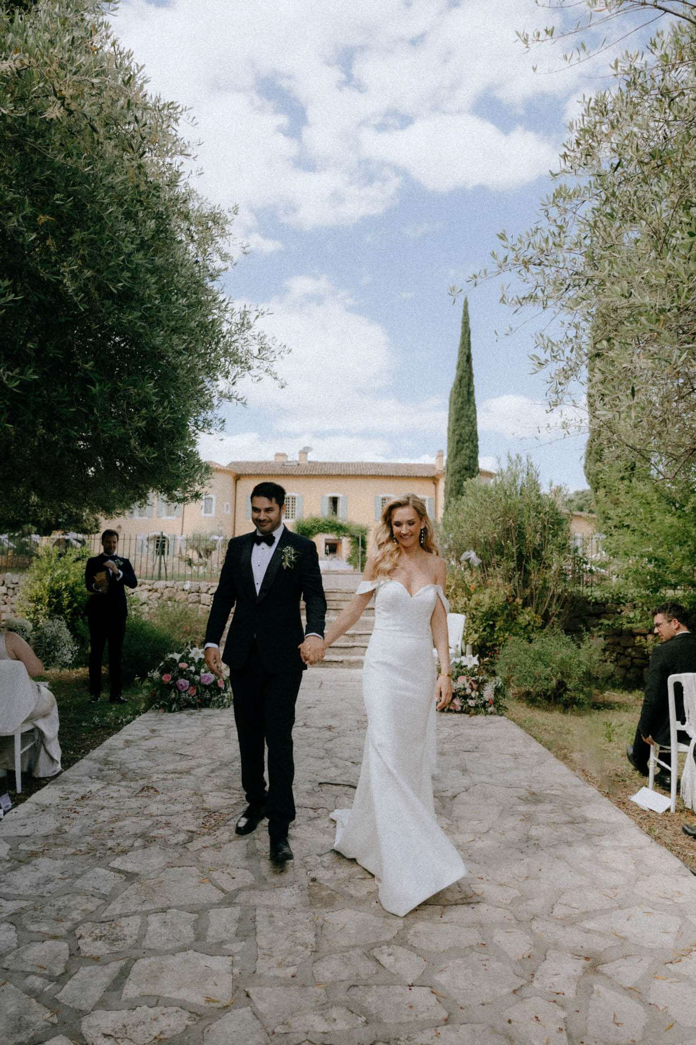 Couple walking down stone aisle after ceremony at ochre bastide with blush and mauve altar florals