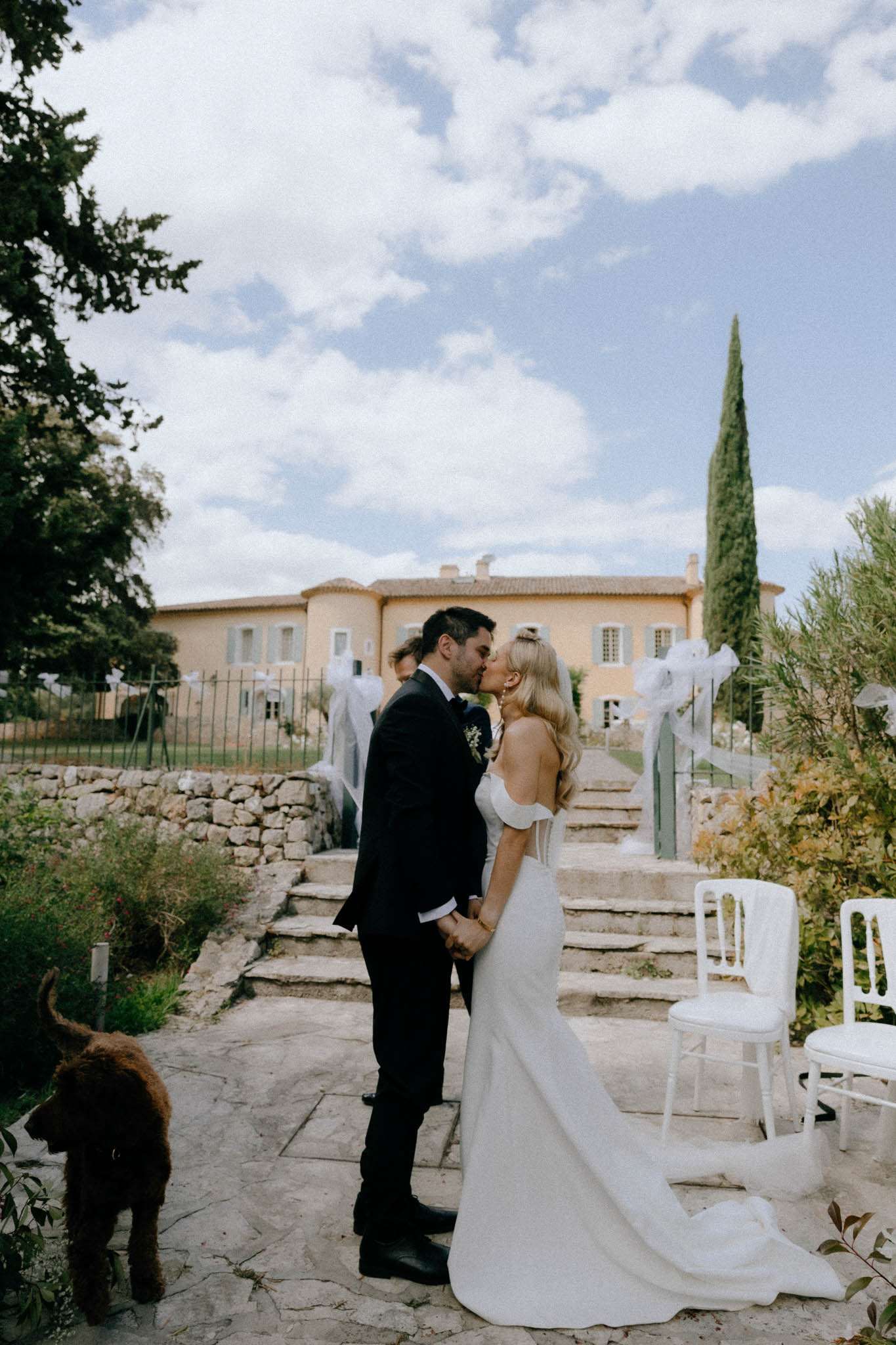 Couple sharing first kiss on Provencal mas terrace with tulle-bowed gate and cypress staircase behind