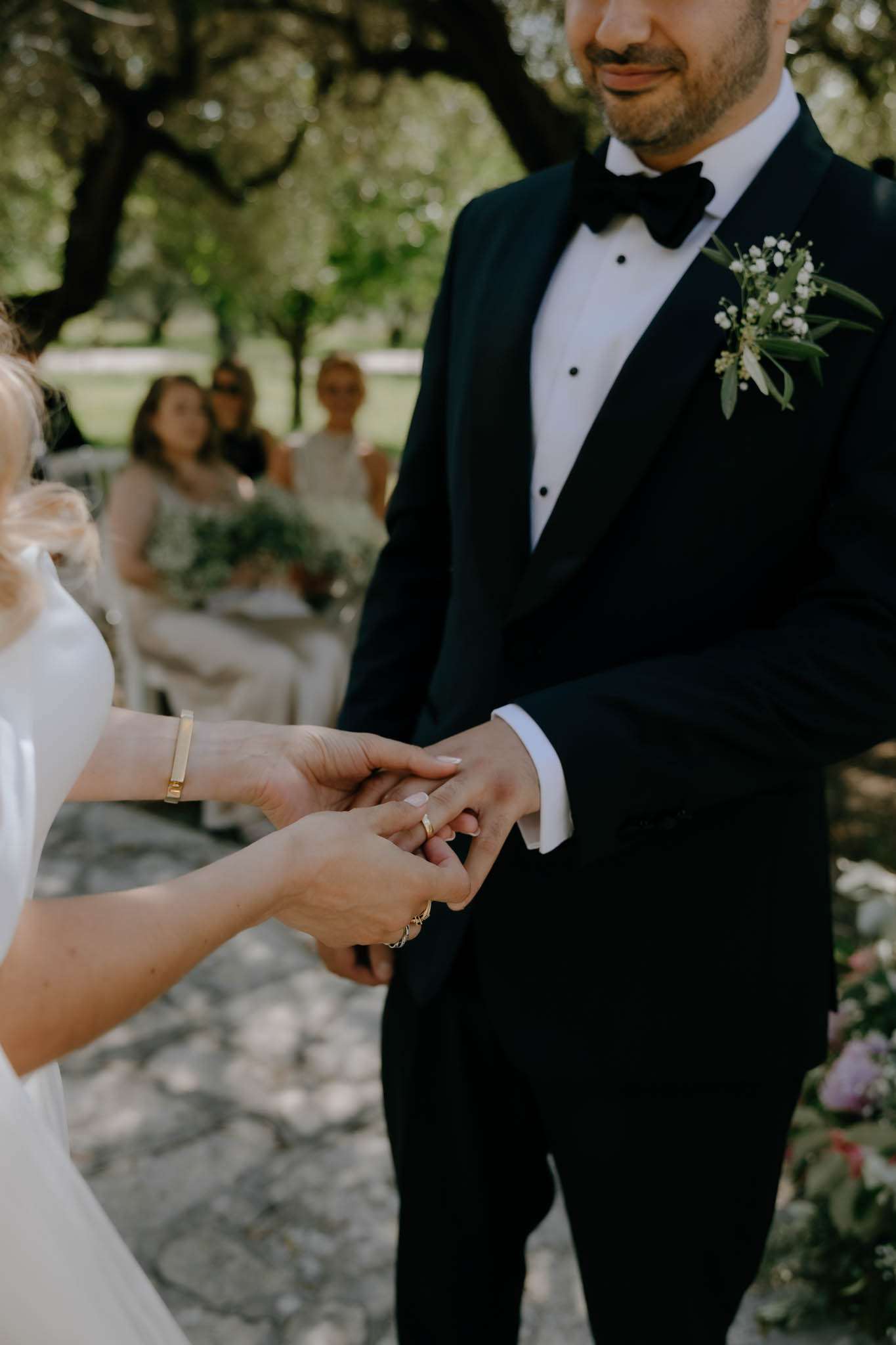 Close-up of bride placing gold wedding band on groom finger during outdoor garden ceremony
