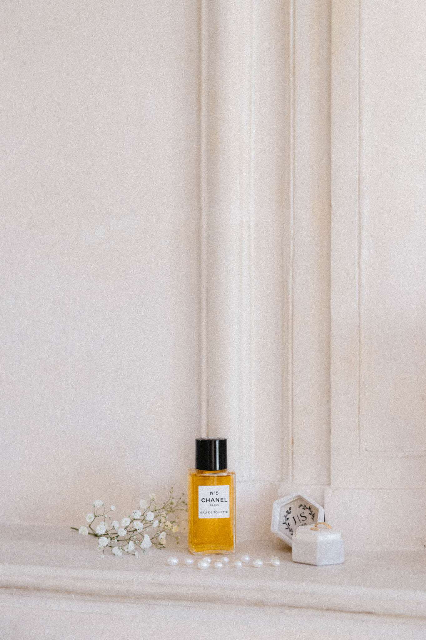 Getting-ready flat lay with Chanel No. 5, pearl beads, baby's breath, and gold wedding bands in velvet ring box