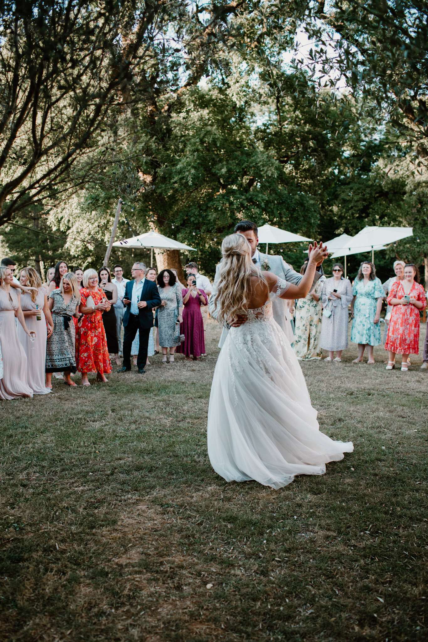 Groom and bride share first dance on lawn as guests circle around in late-afternoon light