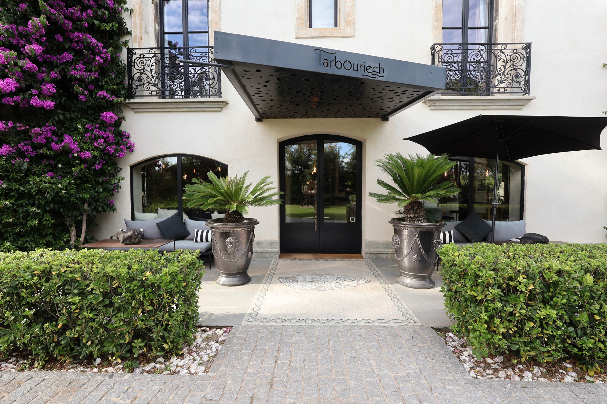 Domaine Tarbouriech entrance facade with wrought-iron balconies, arched doors, and cycas palm urns