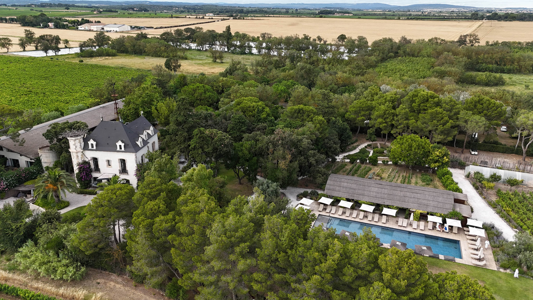 Aerial view of a white-rendered chateau estate with pool, vineyards, and kitchen garden