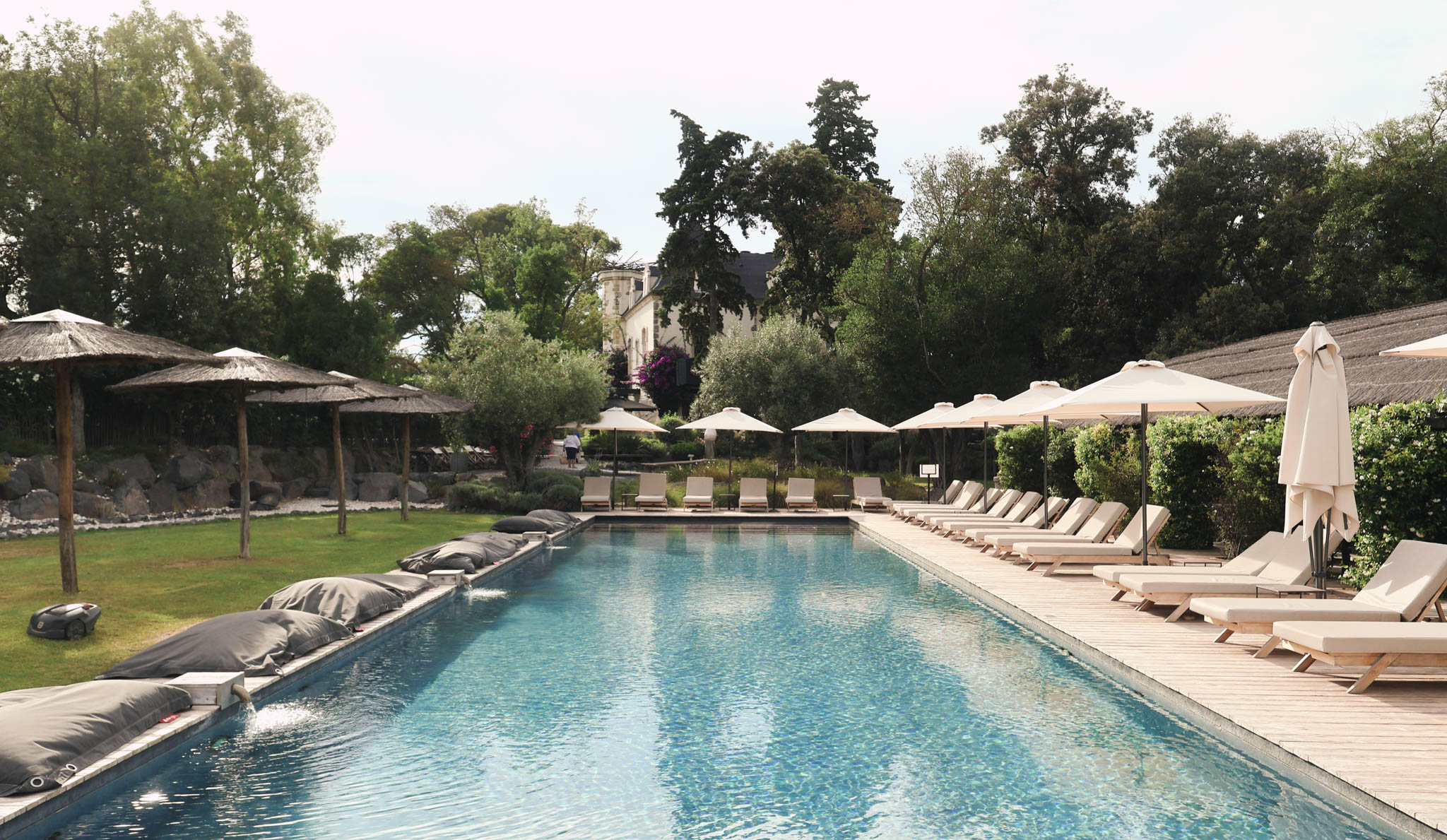 Chateau swimming pool with wooden sun loungers and parasols on deck terrace, main building in background