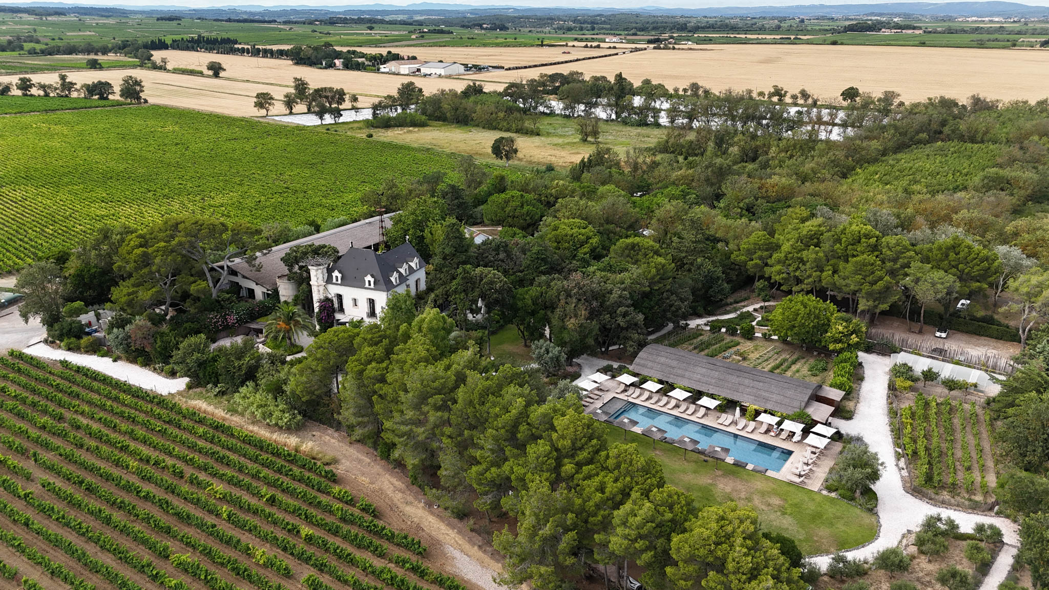 Aerial drone view of French wine estate with white manor house, pool, event barn, and surrounding vineyards
