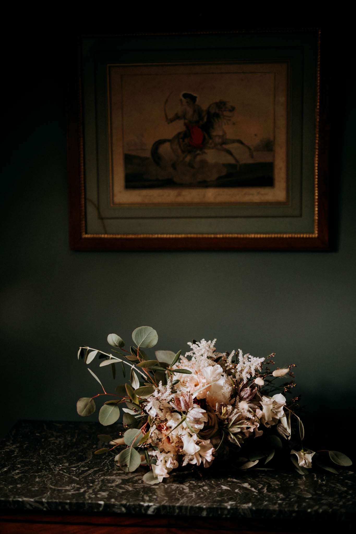 Garden-style bouquet of blush peonies, peach blooms, and trailing eucalyptus on dark marble surface