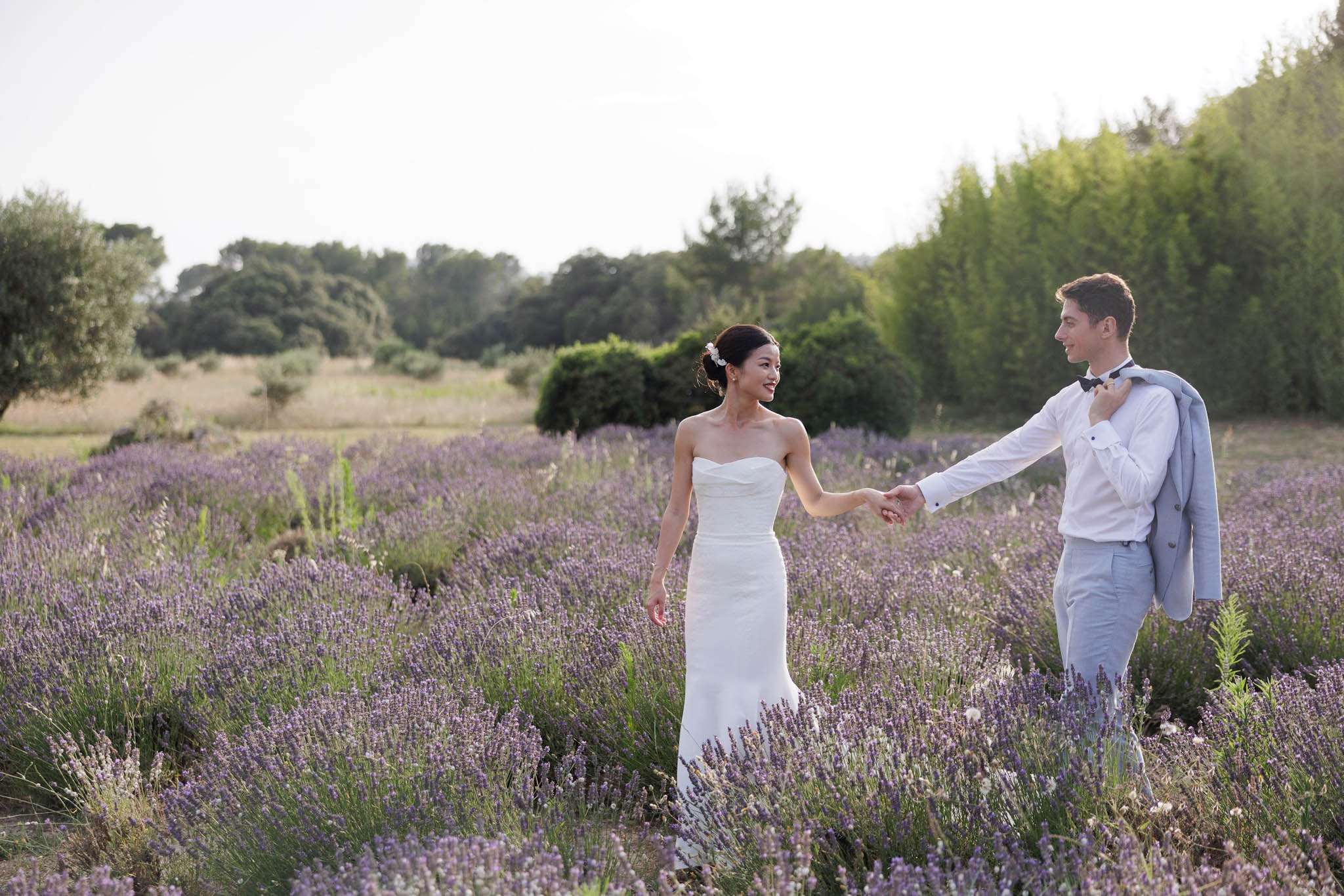 Bride and groom hold hands walking through blooming lavender field in late afternoon light
