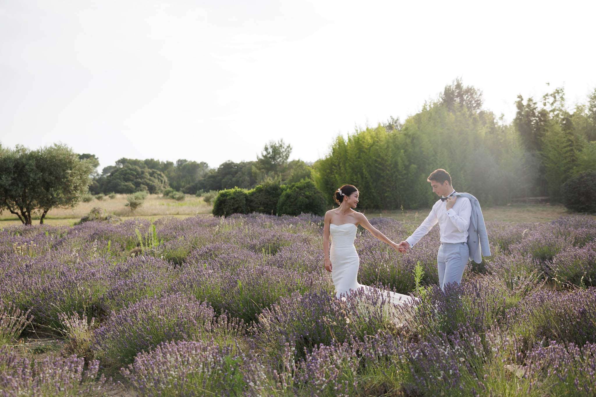Bride and groom walking hand-in-hand through blooming lavender rows in a Provencal landscape