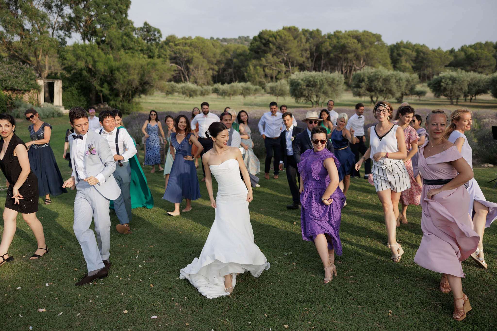 Wedding guests and couple dancing together on lawn with lavender rows and olive trees in background