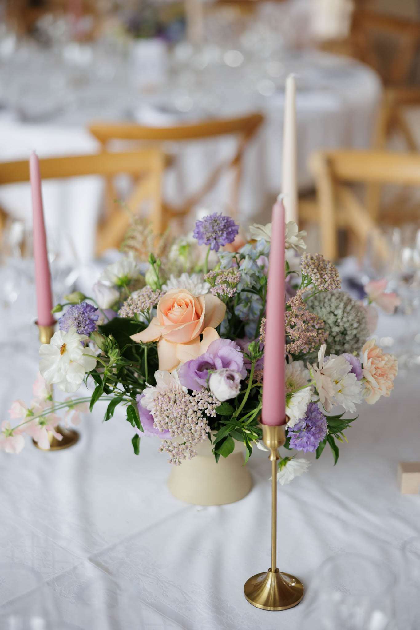 Reception table centrepiece with peach roses, lavender lisianthus, and dusty rose taper candles in brass holders