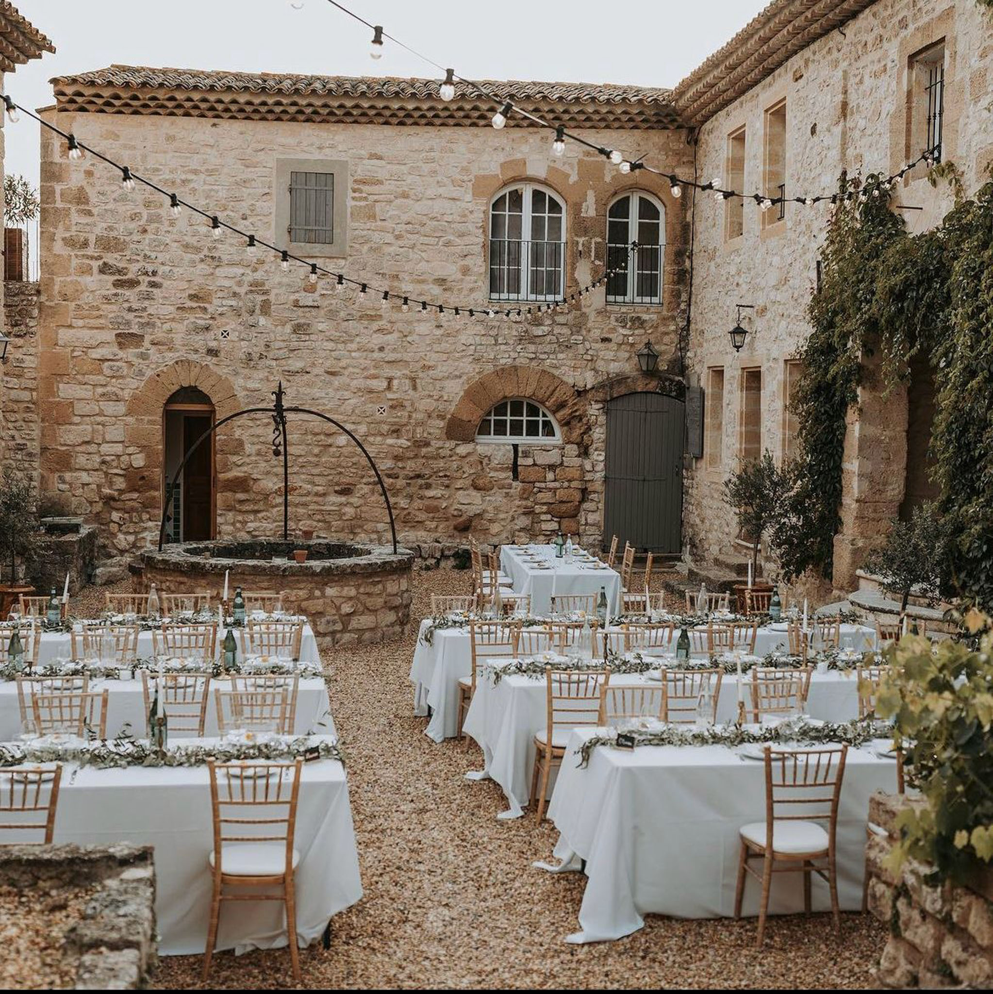 Reception tables with eucalyptus garlands and gold chiavari chairs in stone courtyard with string lights overhead