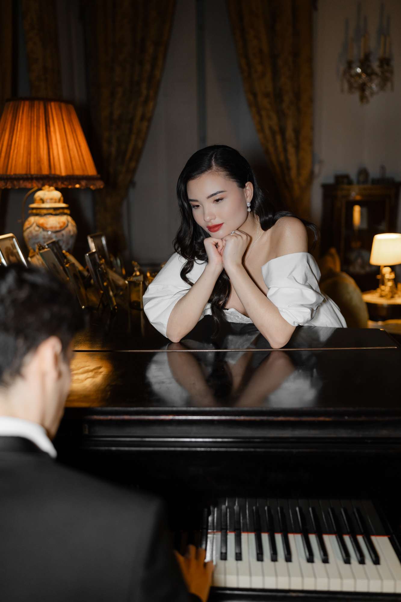 Bride and groom seated at grand piano in elegant interior with amber lighting and gold curtains