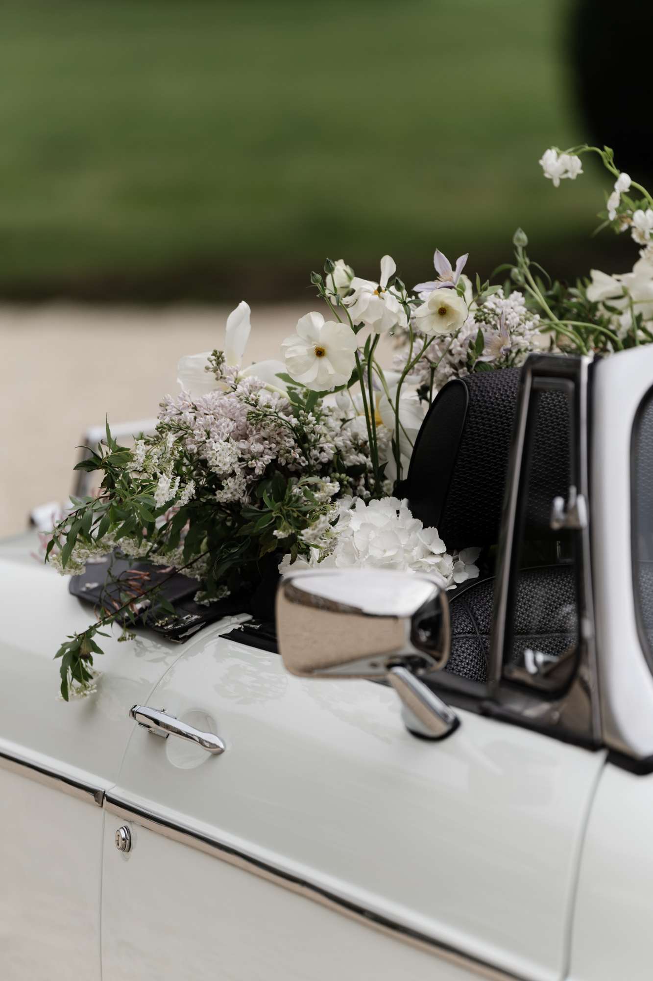 Floral arrangement of white cosmos, daisies, and soft mauve Queen Anne's lace on hood of white vintage car
