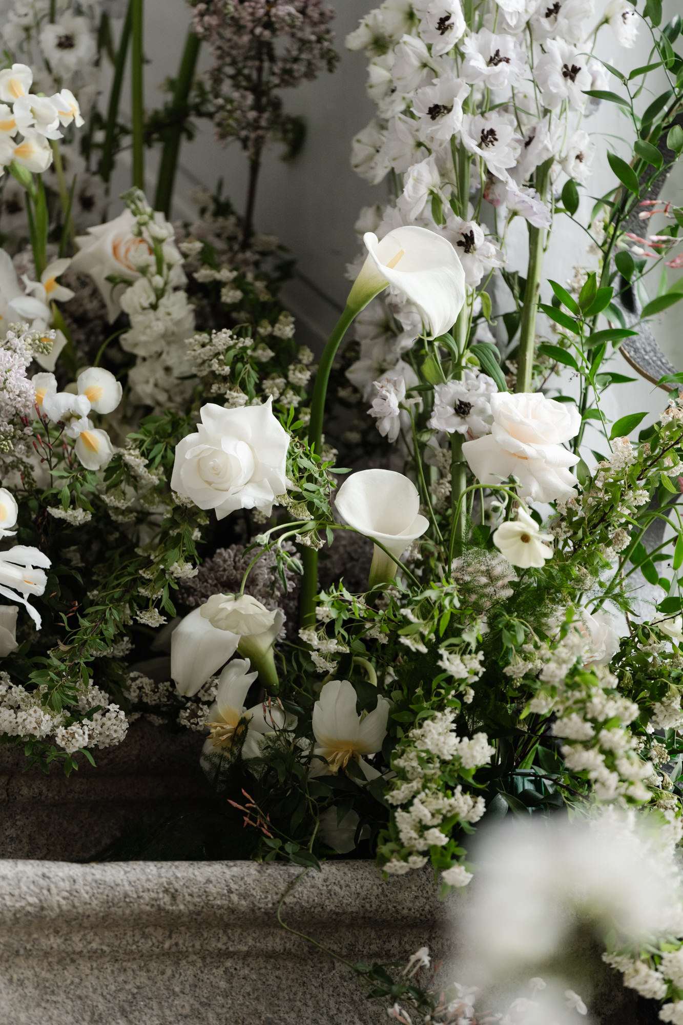 Close-up of white bridal floral arrangement with calla lilies, roses, ranunculus, and baby's breath