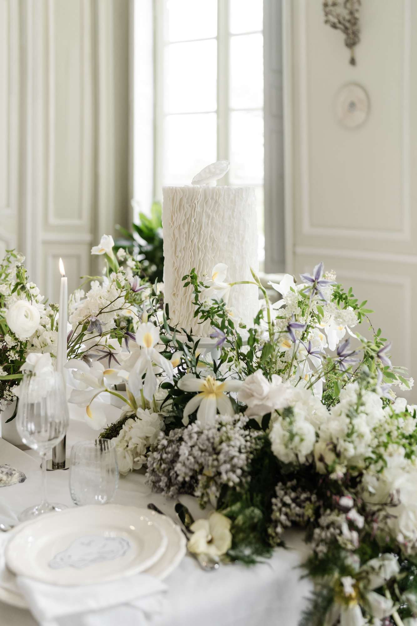 Reception tablescape with white feather cake topper, white anemones and soft lavender florals beside lit candle