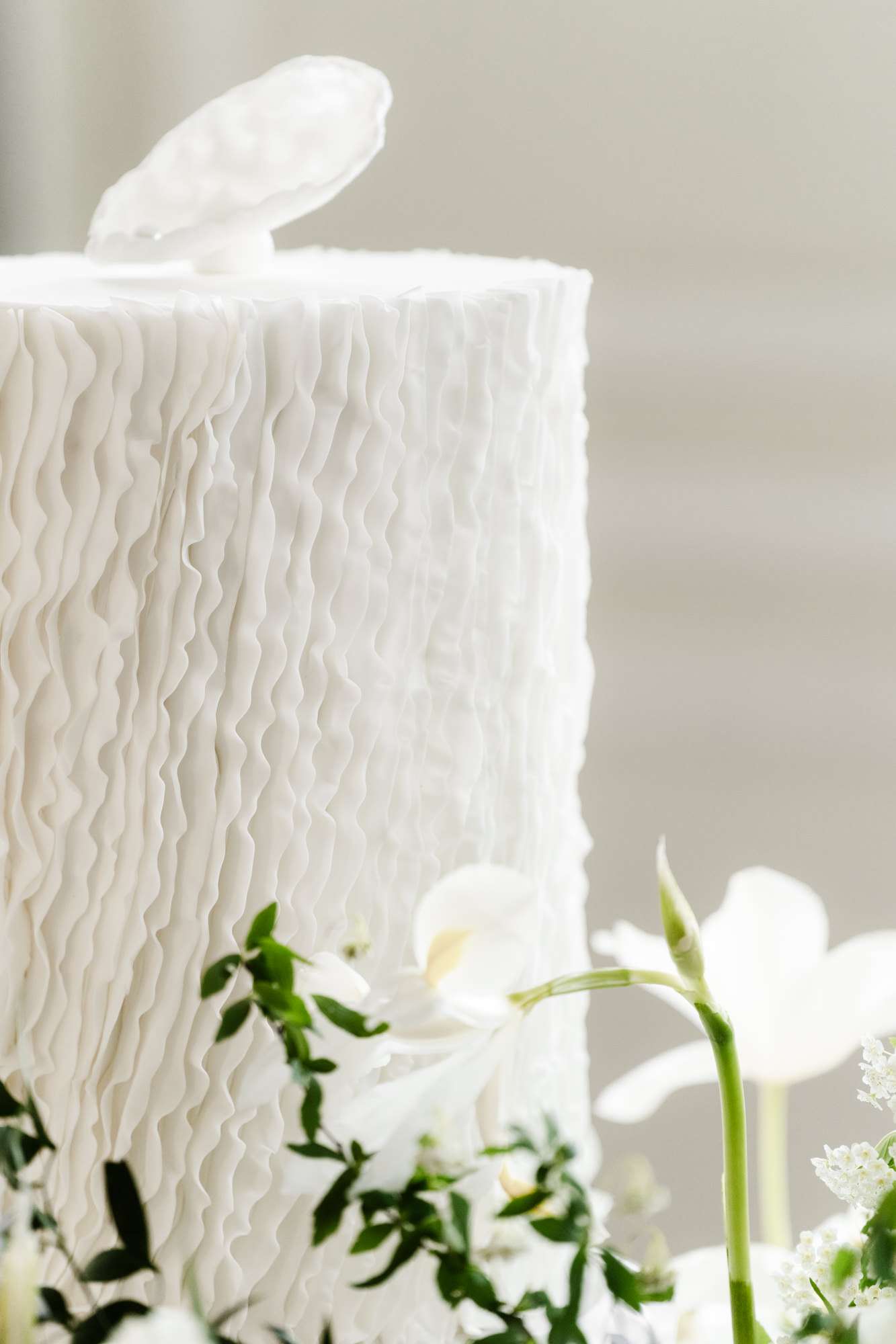 Single-tier ivory buttercream wedding cake with wave piping topped with white sugar flower, fresh orchids at base