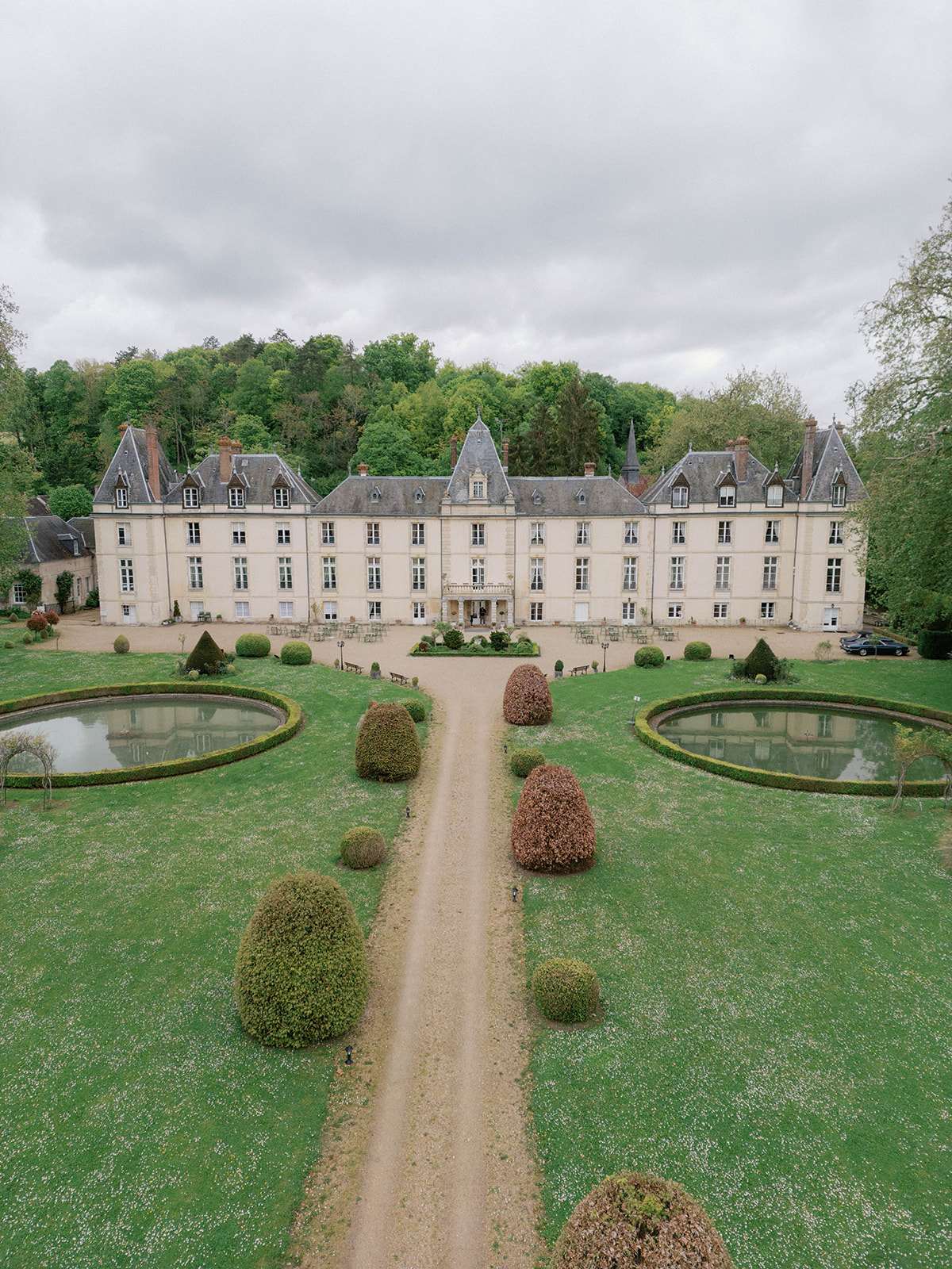 Aerial drone view of French chateau with mansard roofs, formal gardens, ornamental ponds and cocktail setup