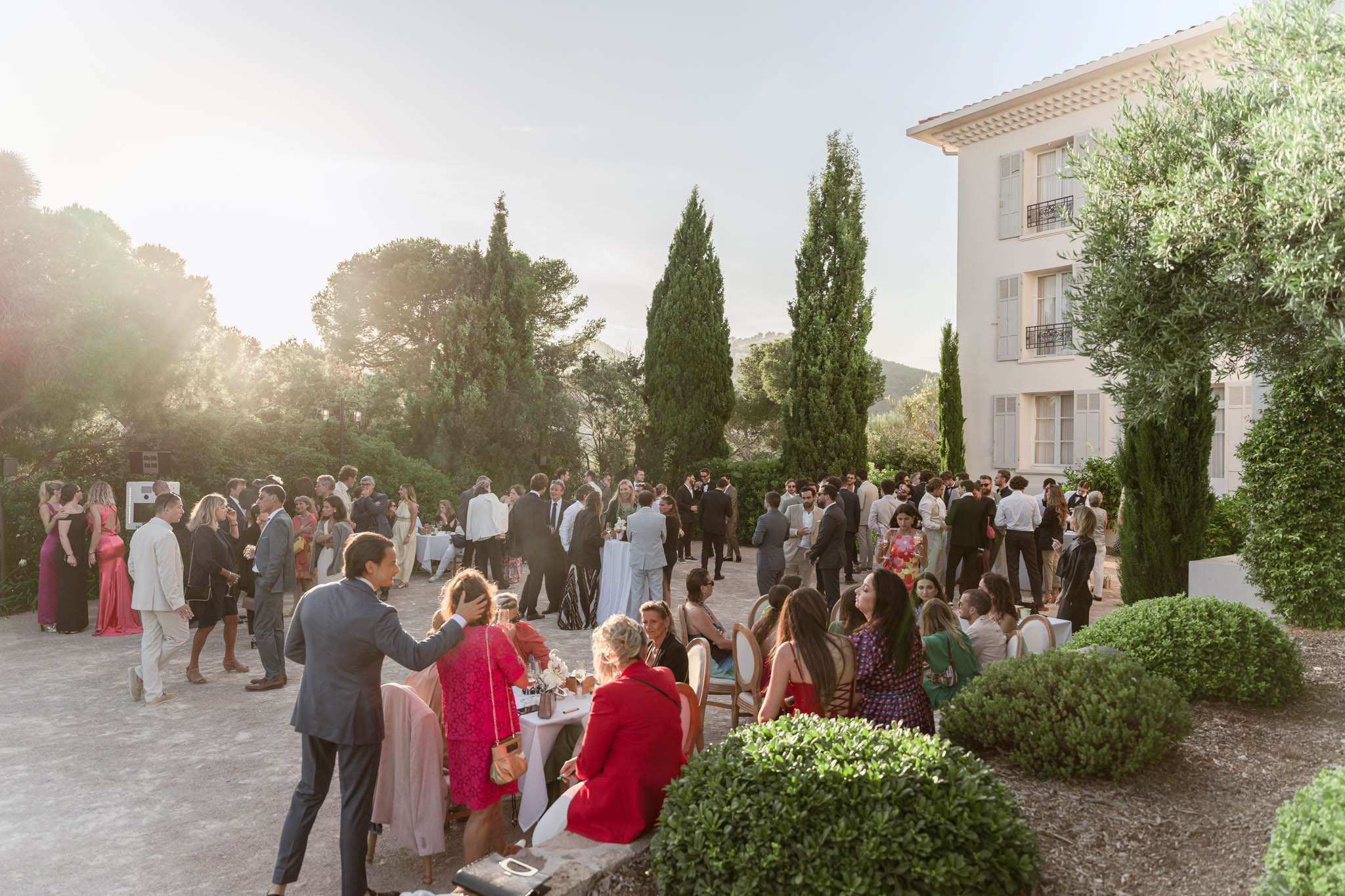 Eighty-plus guests mingle at cocktail tables on Provencal manor courtyard in golden-hour light