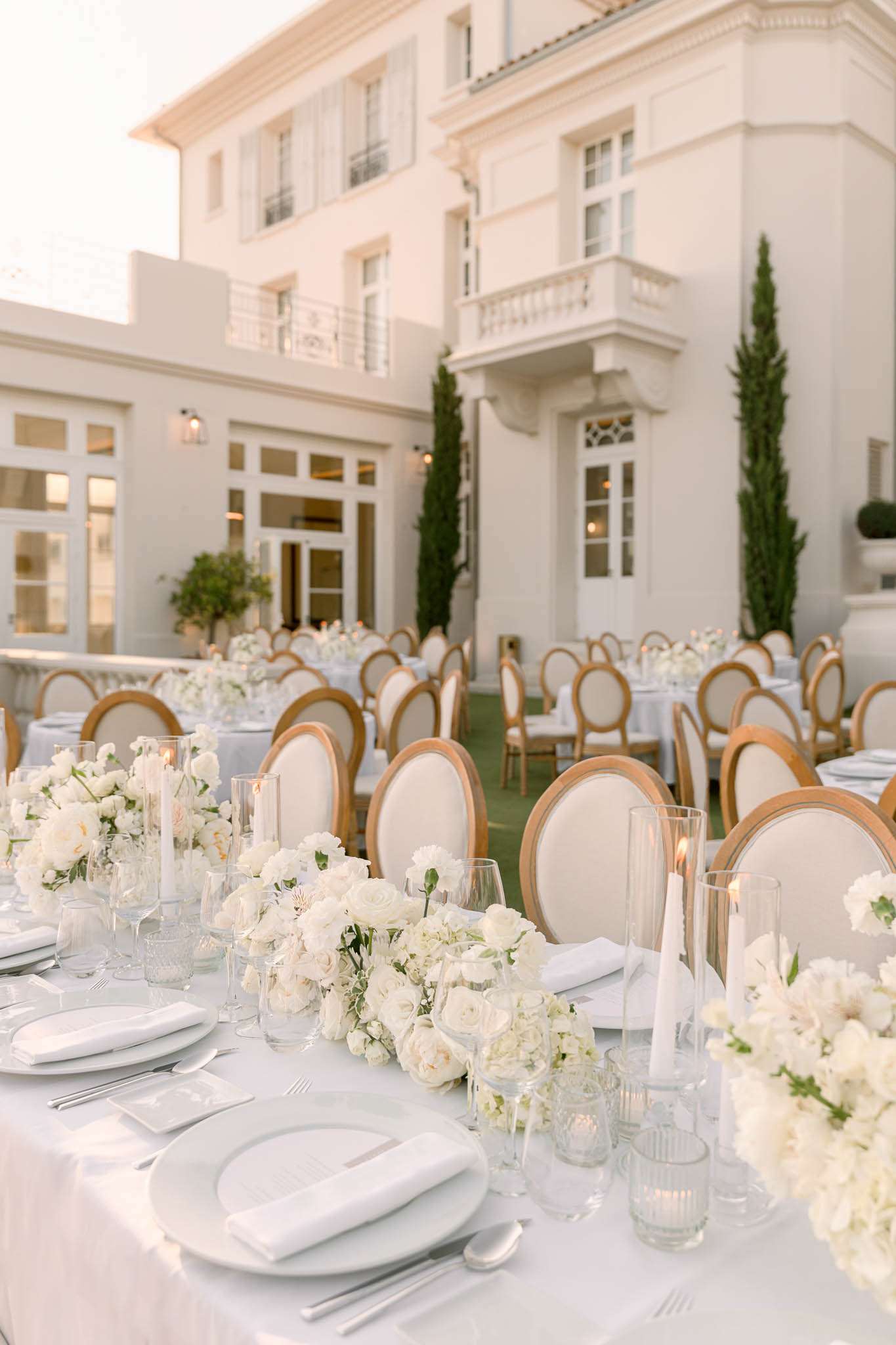 Outdoor reception on villa terrace with long head table, white rose runners, gold chairs, and round guest tables