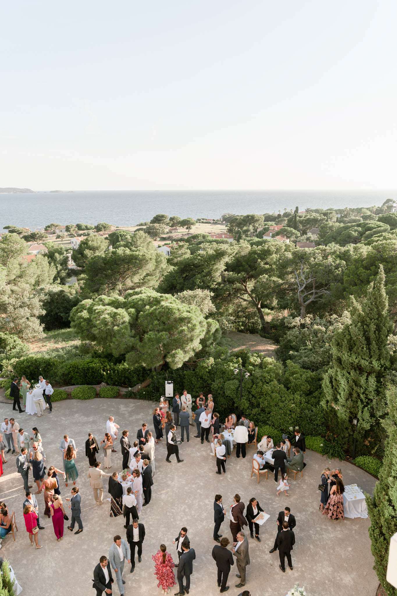 Elevated view of guests mingling on a stone terrace during cocktail hour overlooking the Mediterranean Sea