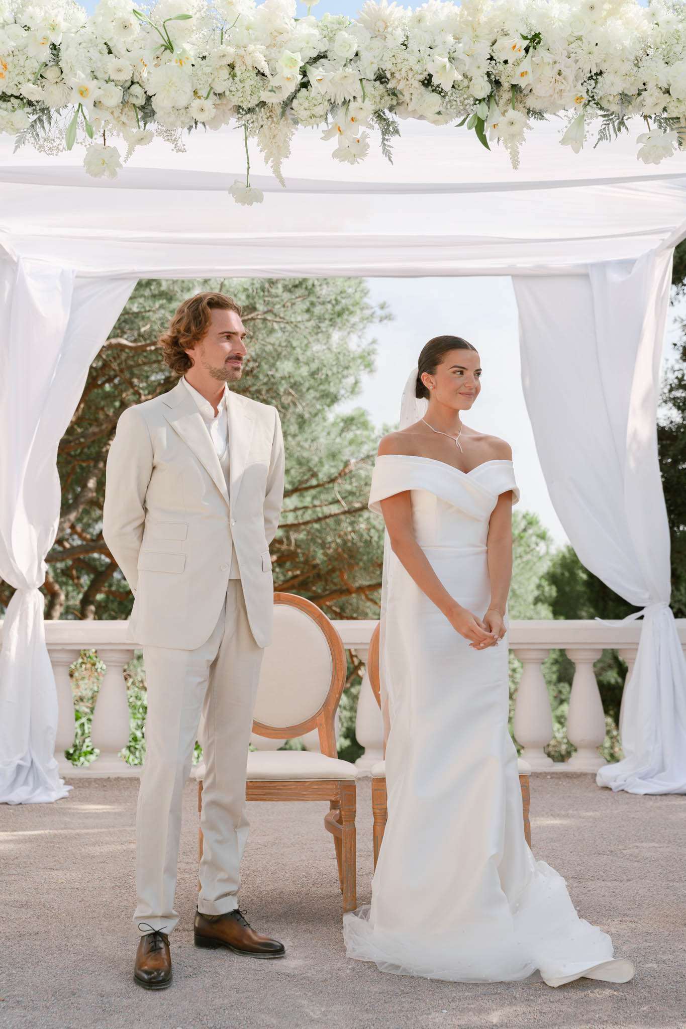 Bride and groom at altar beneath white fabric canopy with white peony and hydrangea floral arrangement
