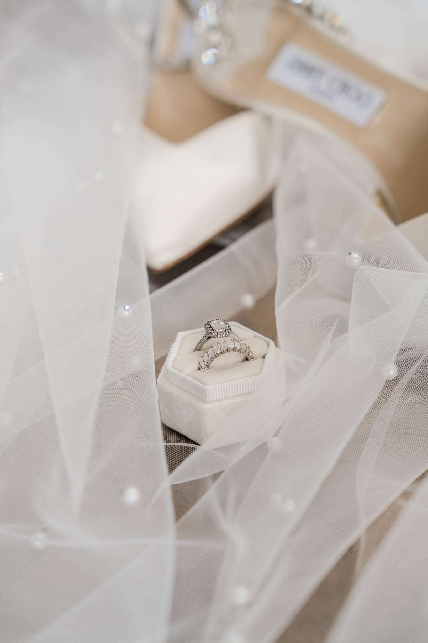 Cushion-cut diamond ring and baguette band in ivory velvet box on pearl-dotted tulle veil