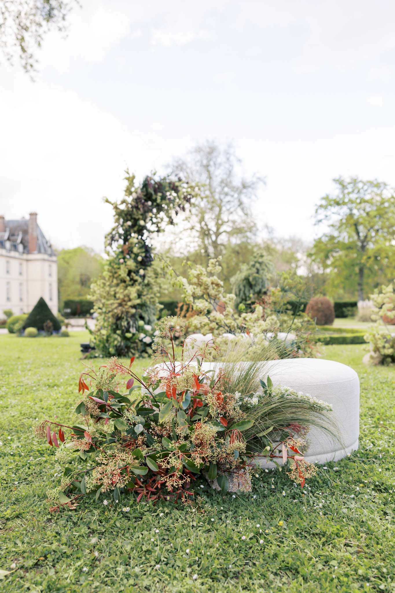 Botanical floral installation with trailing greenery coral flowers and cream blooms beside white ottoman on lawn