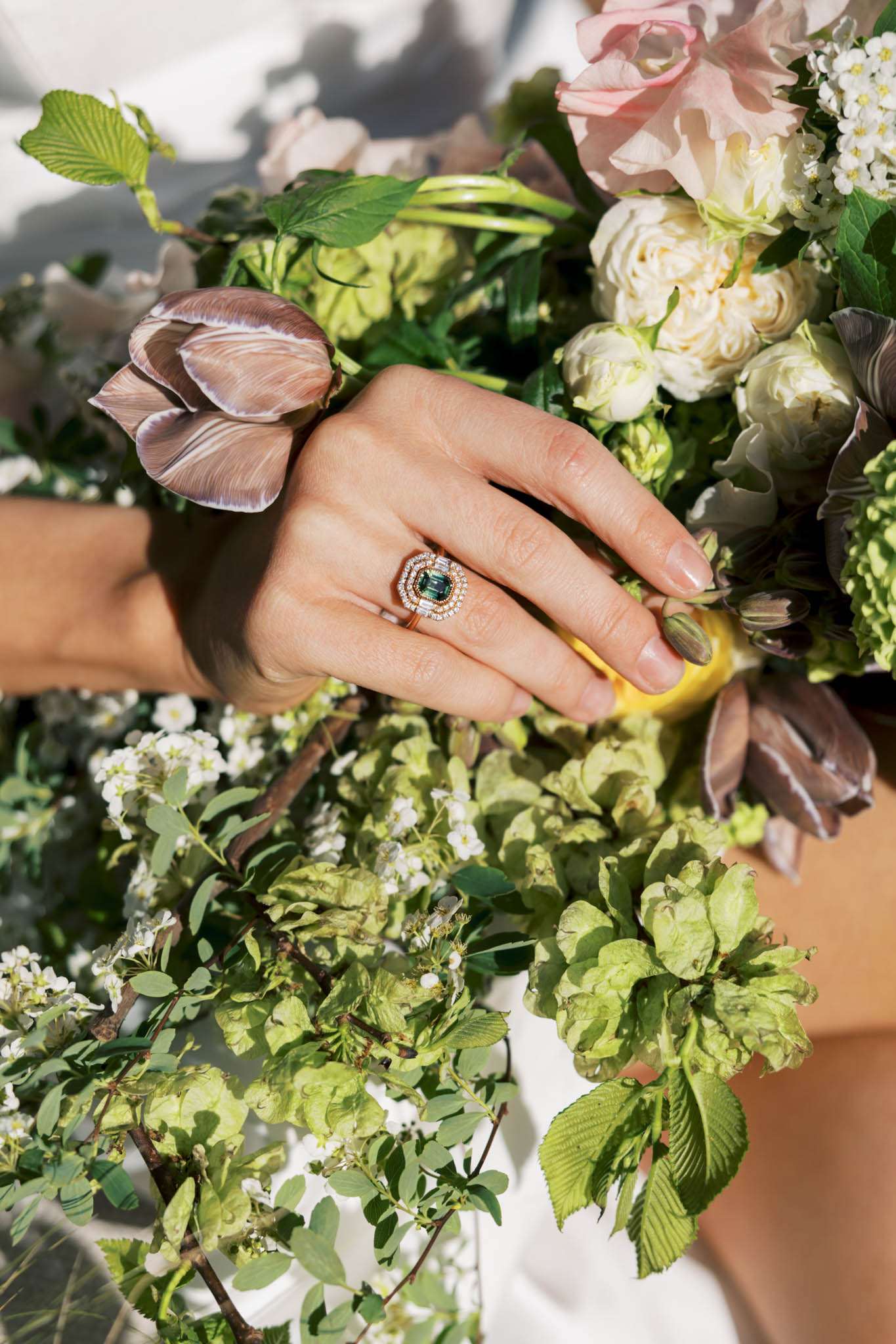 Close-up of bride's emerald engagement ring against a garden-style bouquet of ivory roses and mauve tulips
