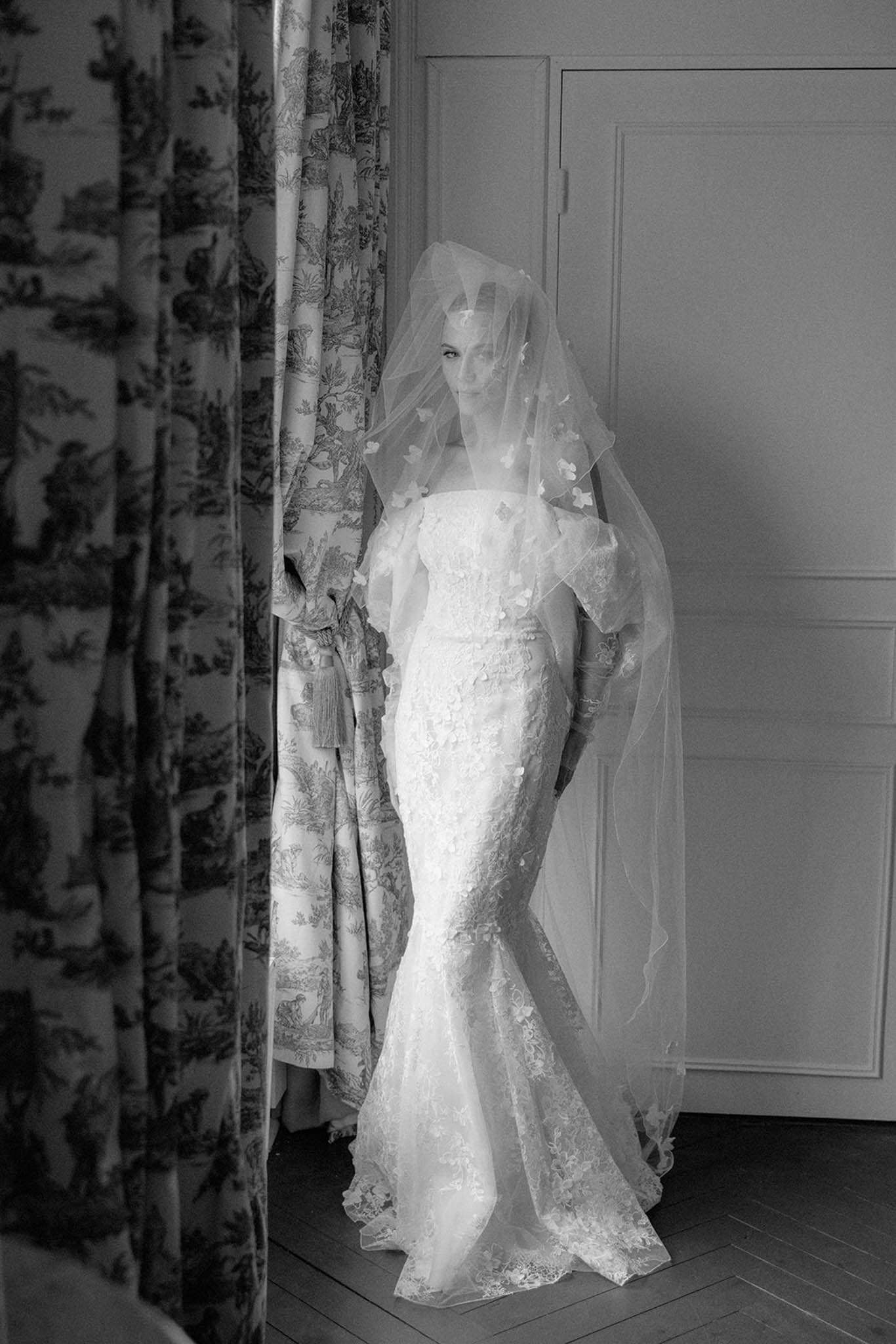 Black and white portrait of bride in fitted lace mermaid gown with applique veil in chateau room