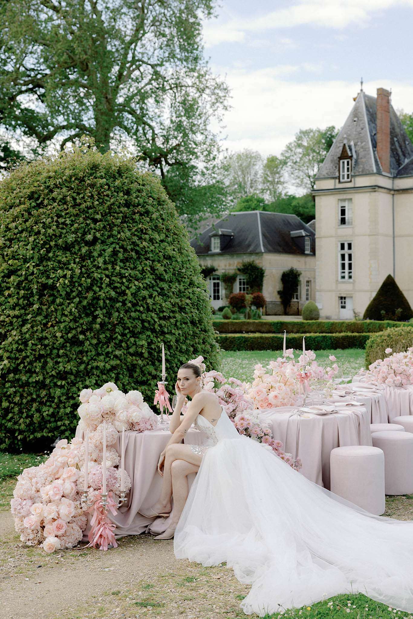 Bride at mauve linen table with cascading blush roses silver candelabras and ottoman seating before chateau
