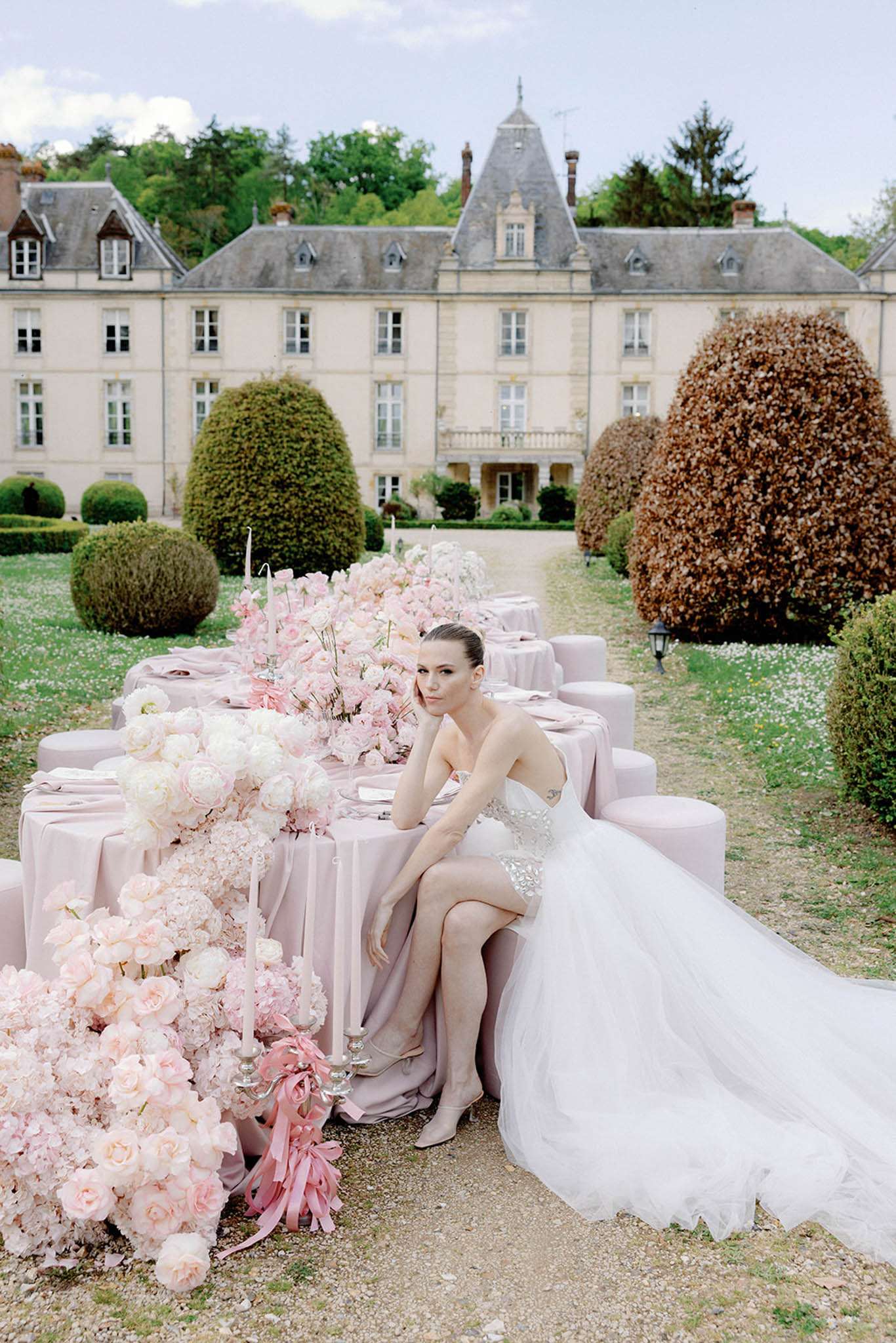 Blush linen table with pink rose runner, silver candelabras, and pink tapers before stone chateau