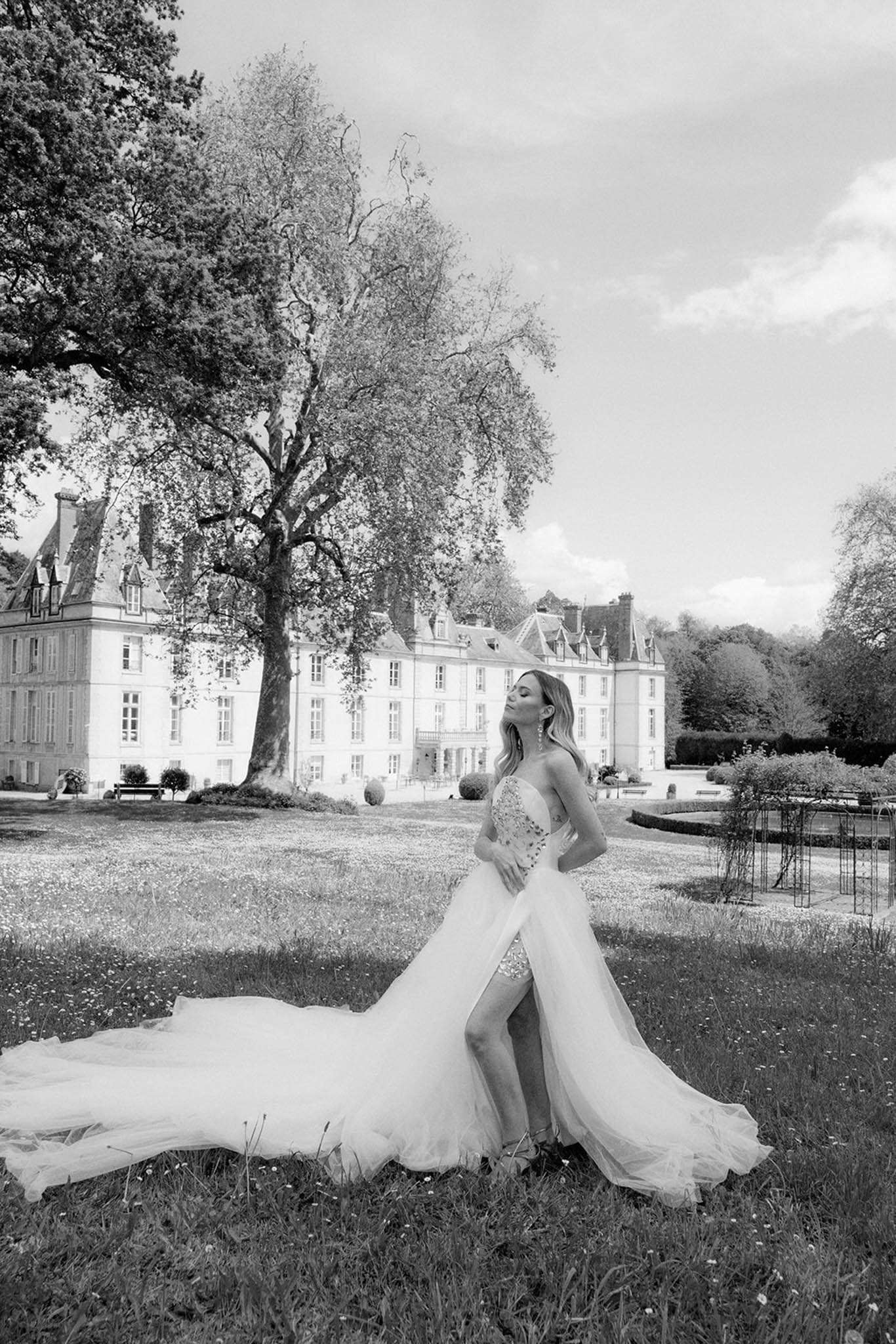 Black and white bridal portrait on chateau lawn, bride in strapless beaded ball gown with dramatic tulle train
