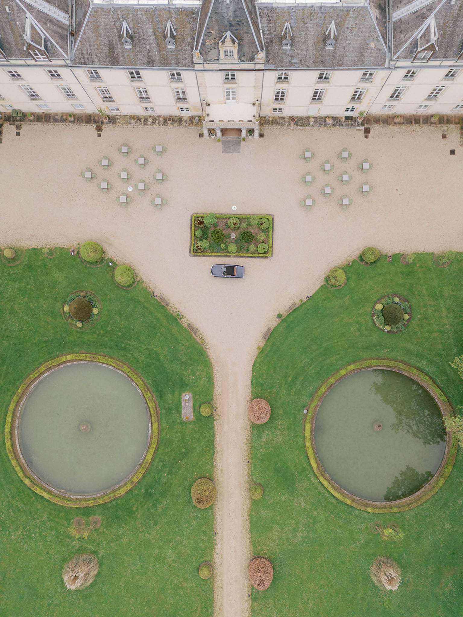Aerial overhead view of chateau with parterre garden ornamental ponds and convertible on gravel drive
