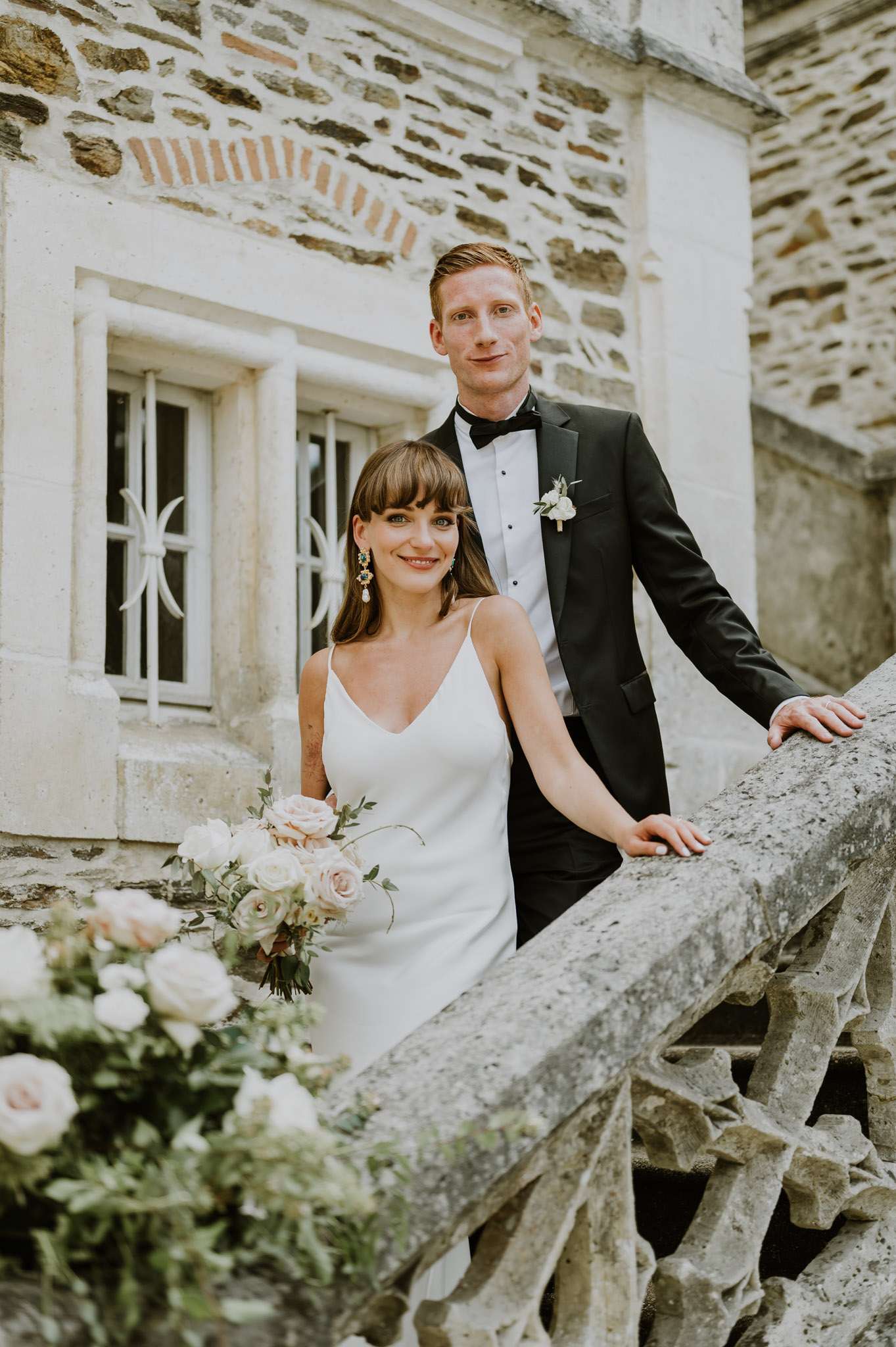 Couple on stone staircase of chateau with bride holding blush and cream rose bouquet