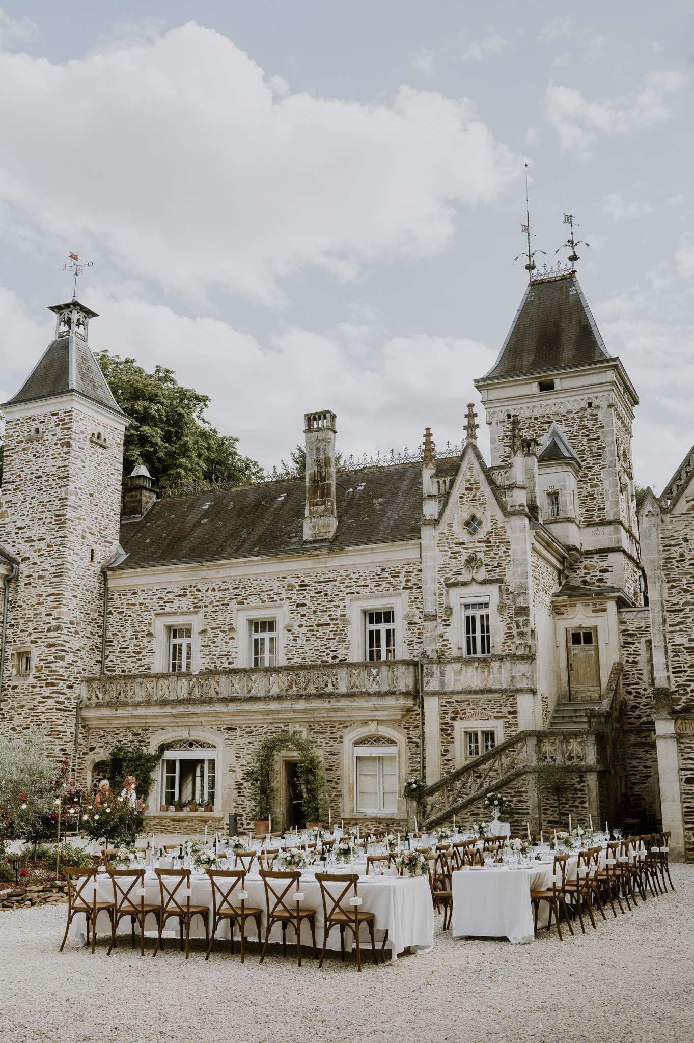 U-shape reception tables with white florals and crossback chairs in Gothic chateau gravel courtyard