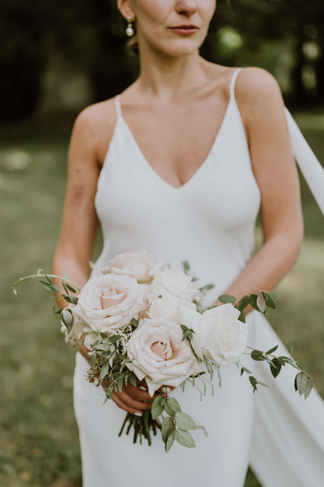 Bride in white slip dress with pearl earrings holding blush and ivory garden rose bouquet