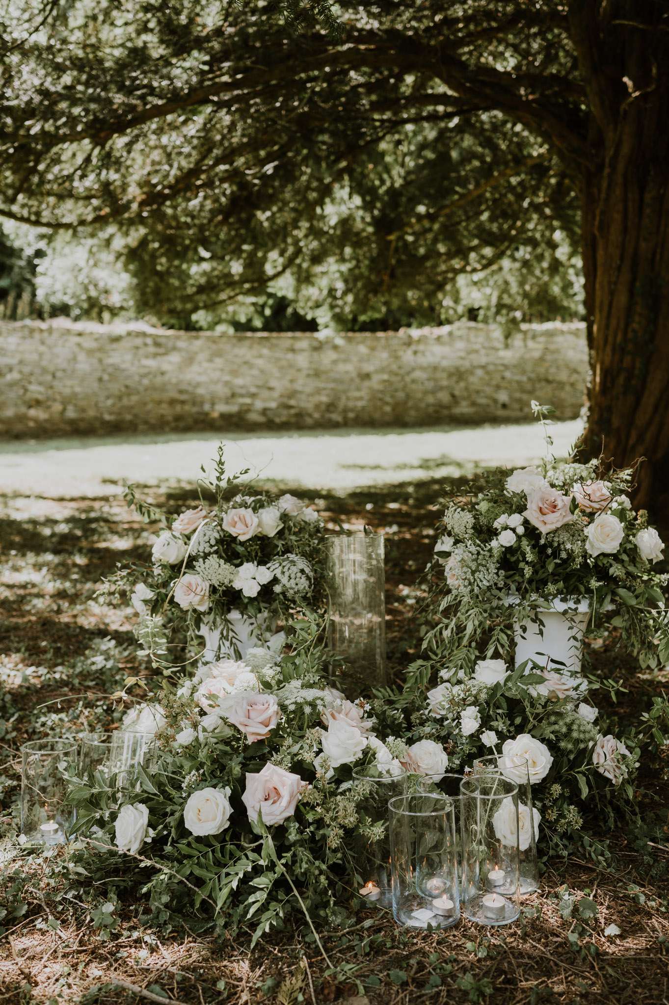 Outdoor ceremony floral installation with greenery-covered hoop wreaths, blush and ivory roses, and hurricane candles