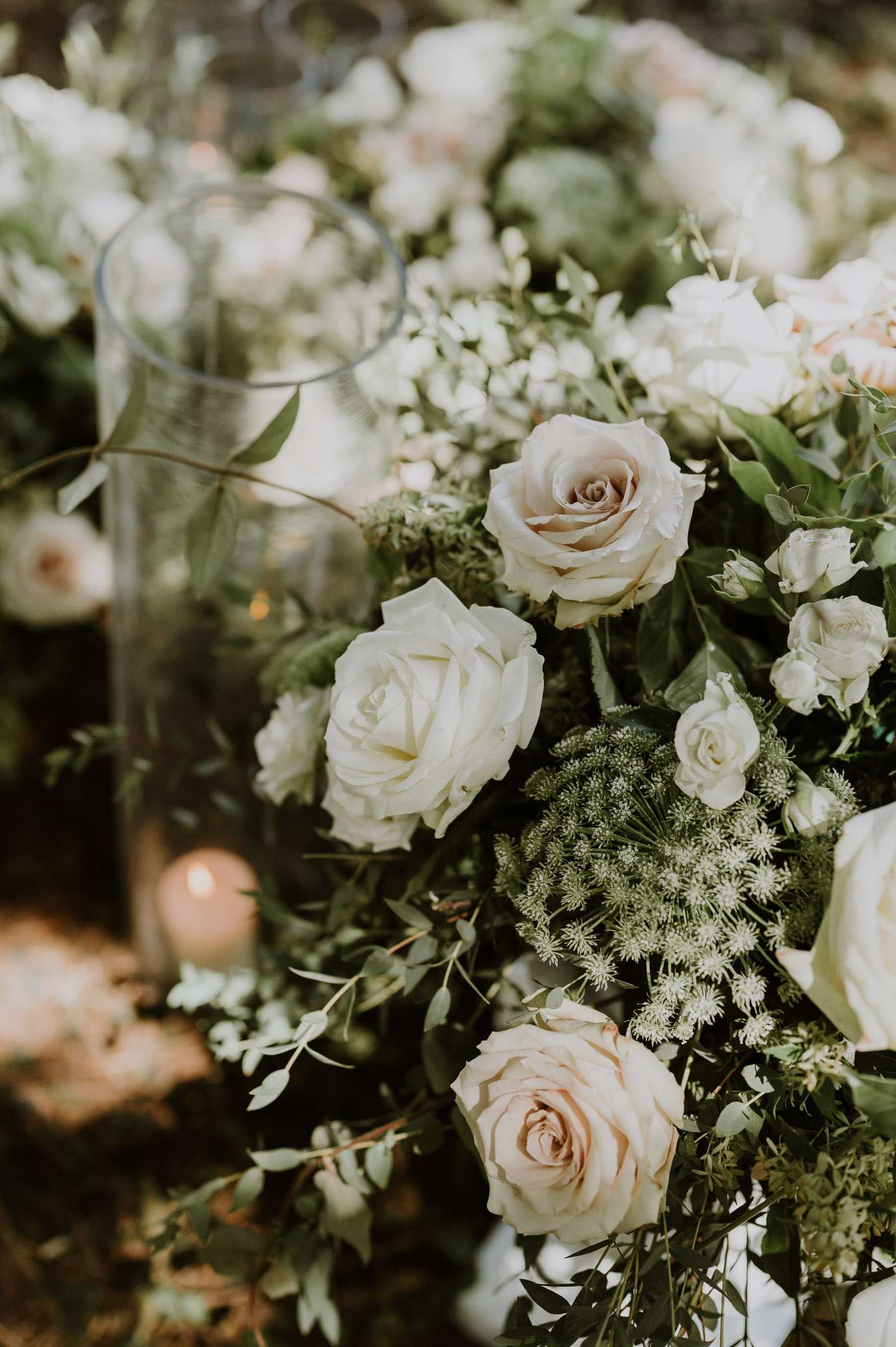 Close-up of ivory and blush roses with eucalyptus and queen anne's lace beside hurricane candle