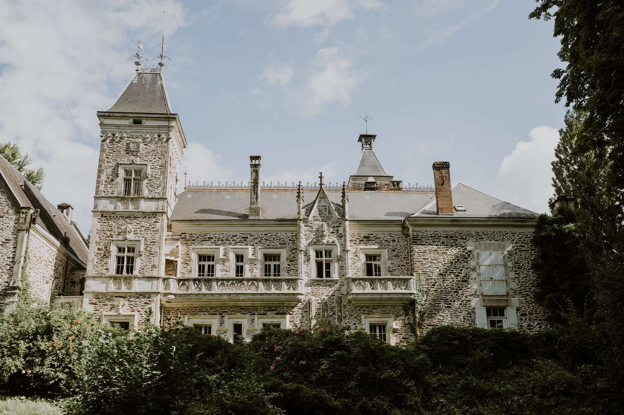 French chateau with corner tower, slate roof, white balustrades, ironwork cresting, and pink flowering plants