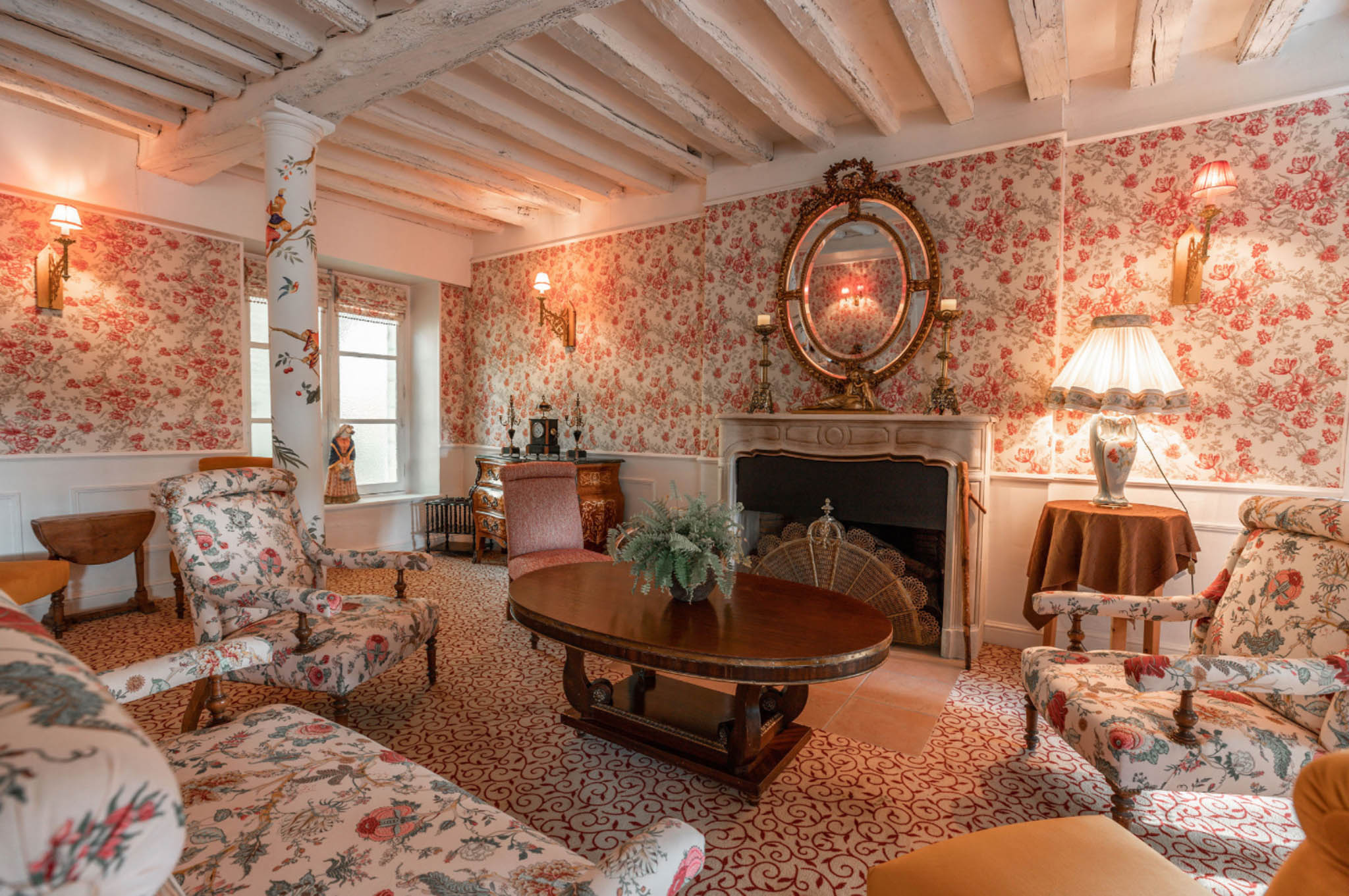 Formal sitting room in a French chateau with floral wallpaper, marble fireplace, and antique armchairs