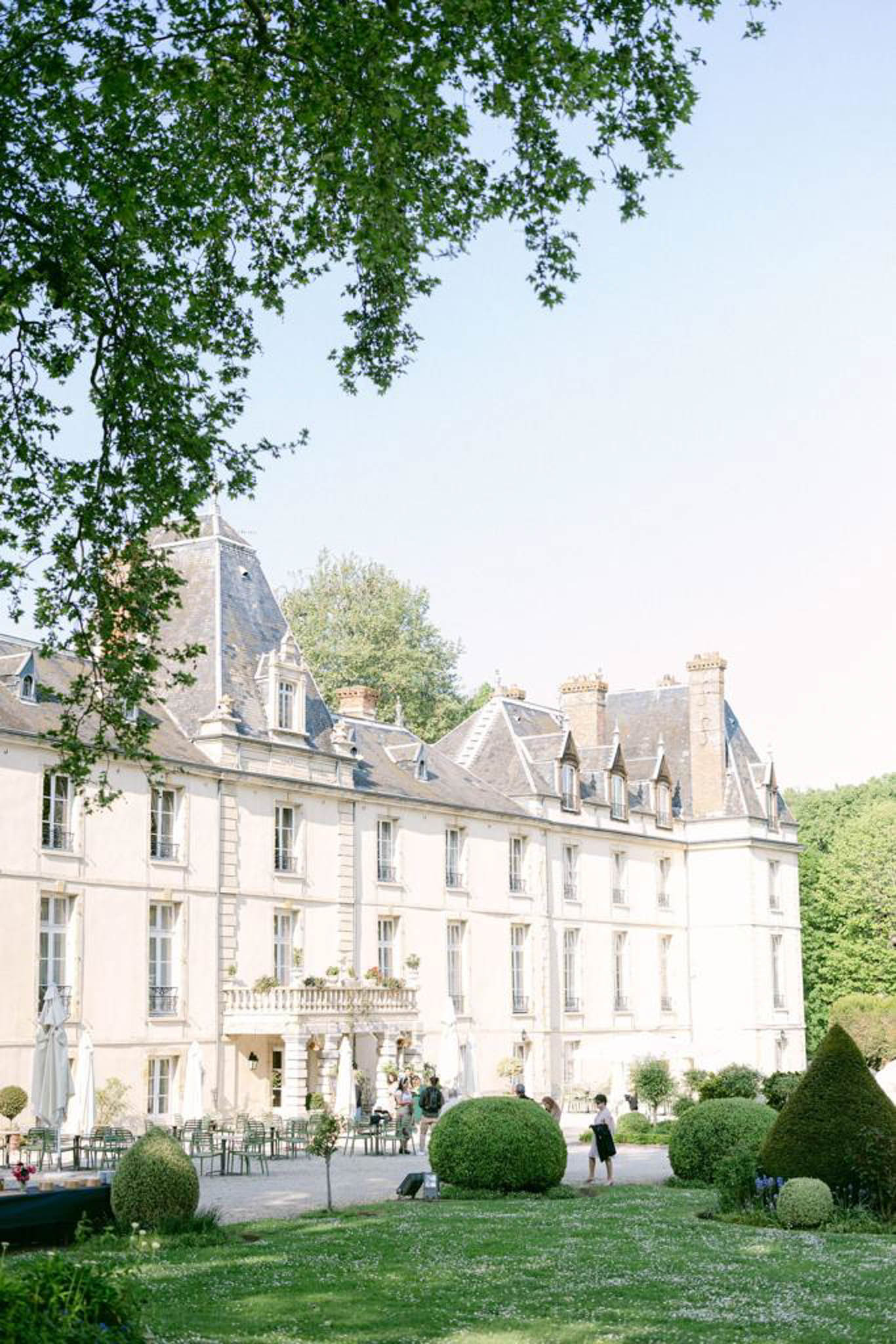 French chateau with cream stone facade and slate mansard roofs with chairs arranged on gravel courtyard