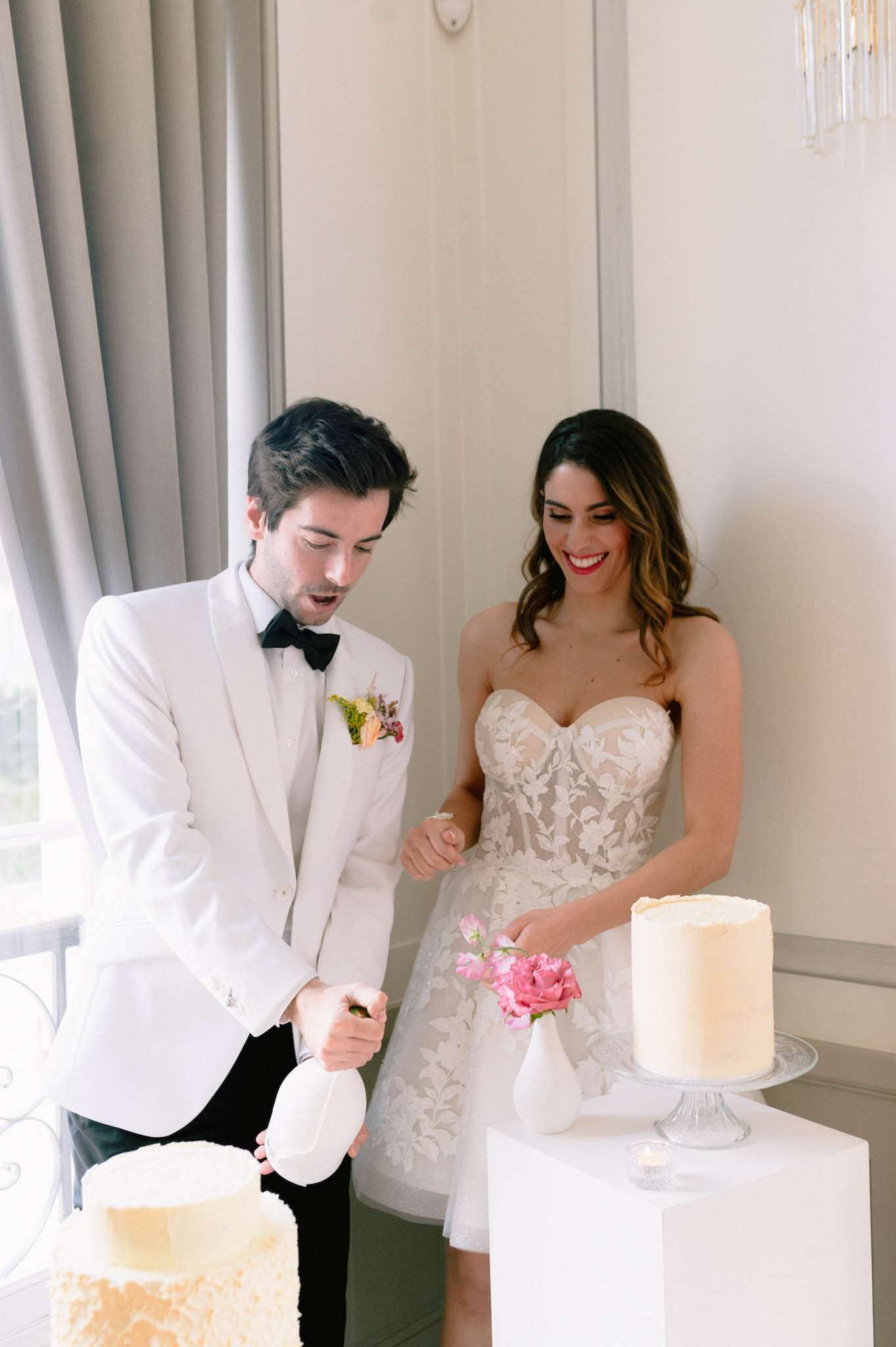 Couple cutting ivory frosted cake with pink roses bride in lace applique gown groom in white tuxedo jacket