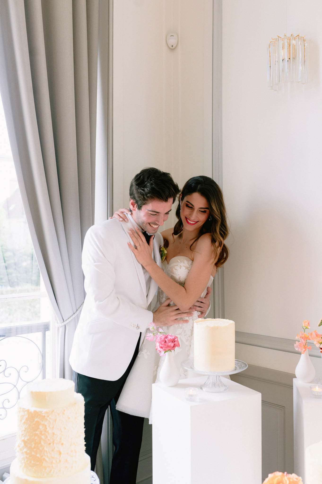 Bride and groom laughing beside ruffled ivory and white wedding cakes at indoor reception display