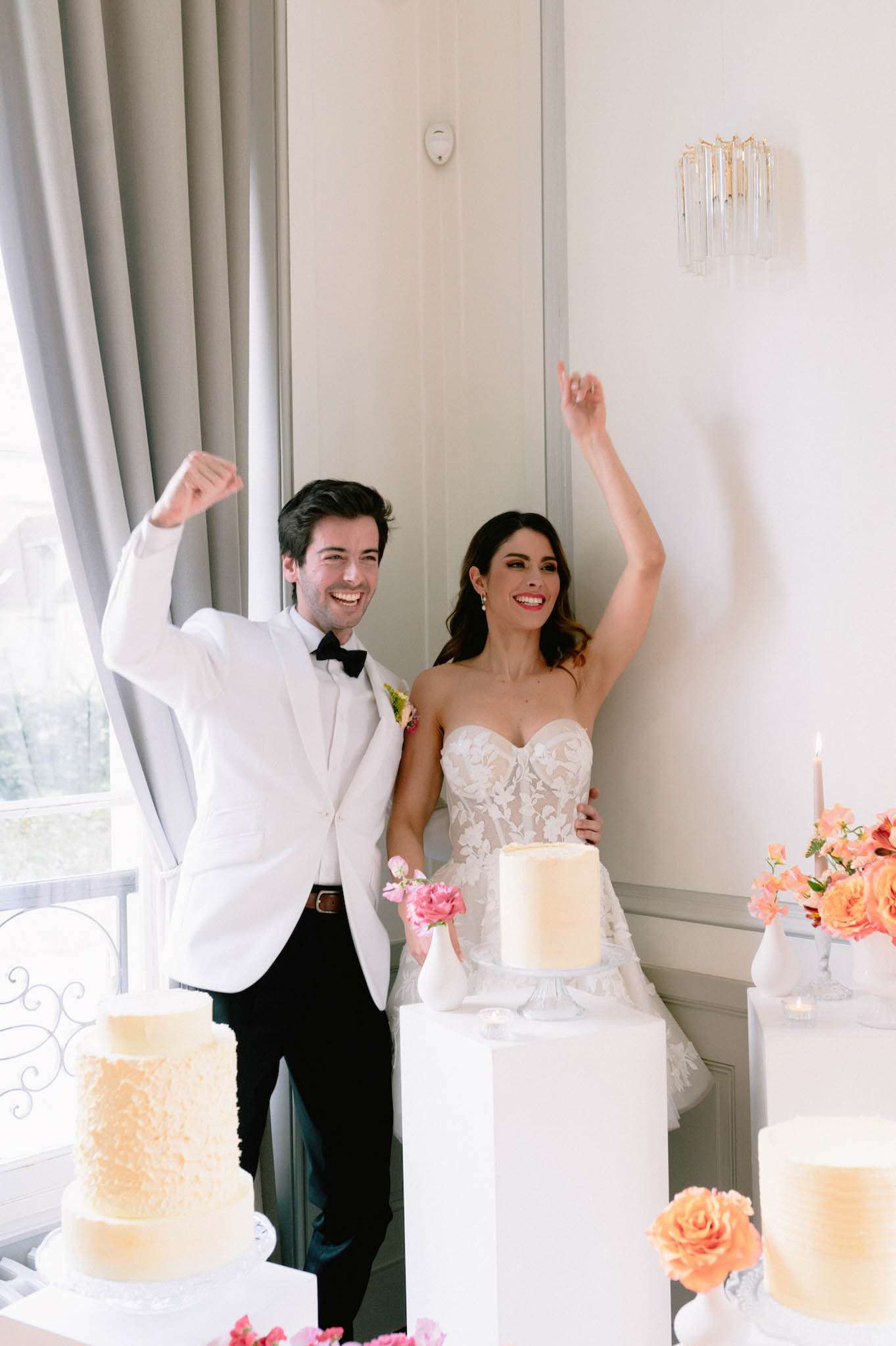 Couple celebrating at multi-cake display with coral and hot pink rose arrangements