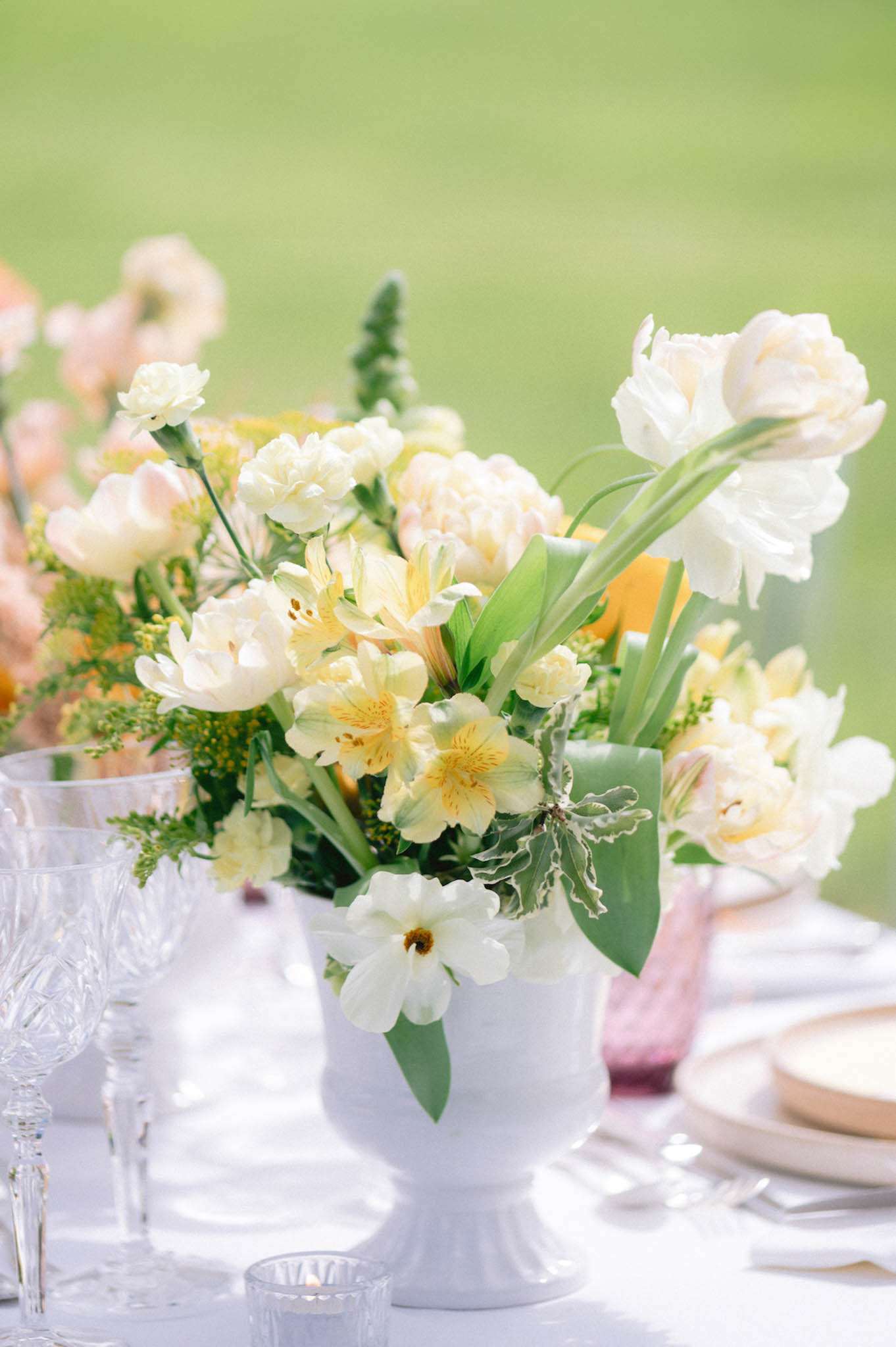 White ceramic urn centerpiece with parrot tulips yellow alstroemeria garden roses and tropical leaves