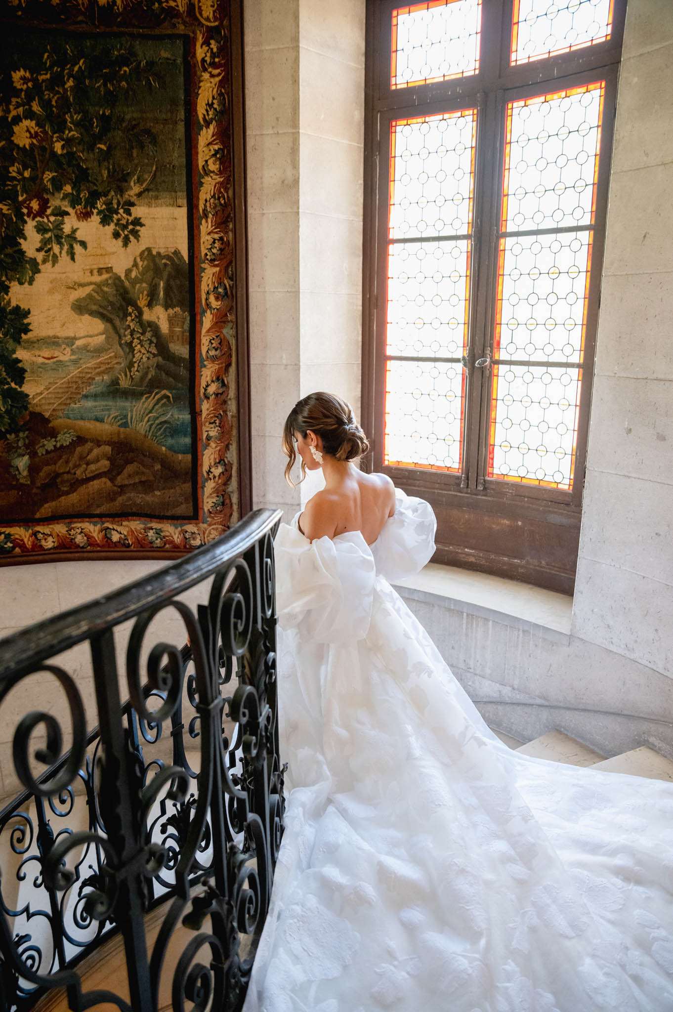 Bride photographed from behind on a stone staircase inside a chateau wearing an off-shoulder ballgown with long train