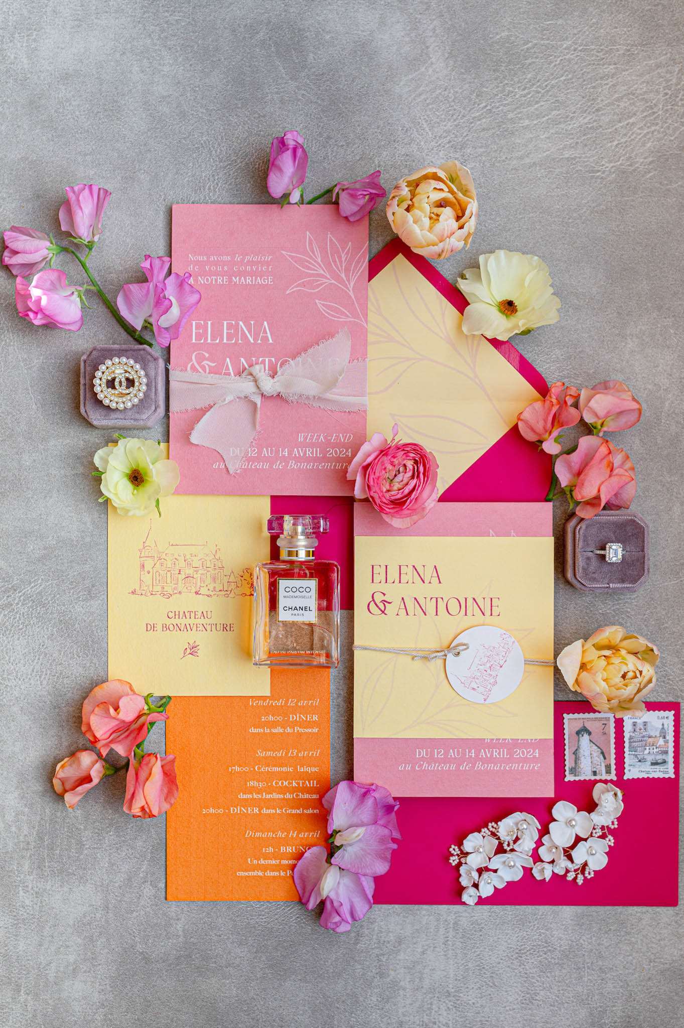 Flat lay of colorful wedding stationery suite with pink ranunculus, peach peonies, Chanel perfume, and engagement ring