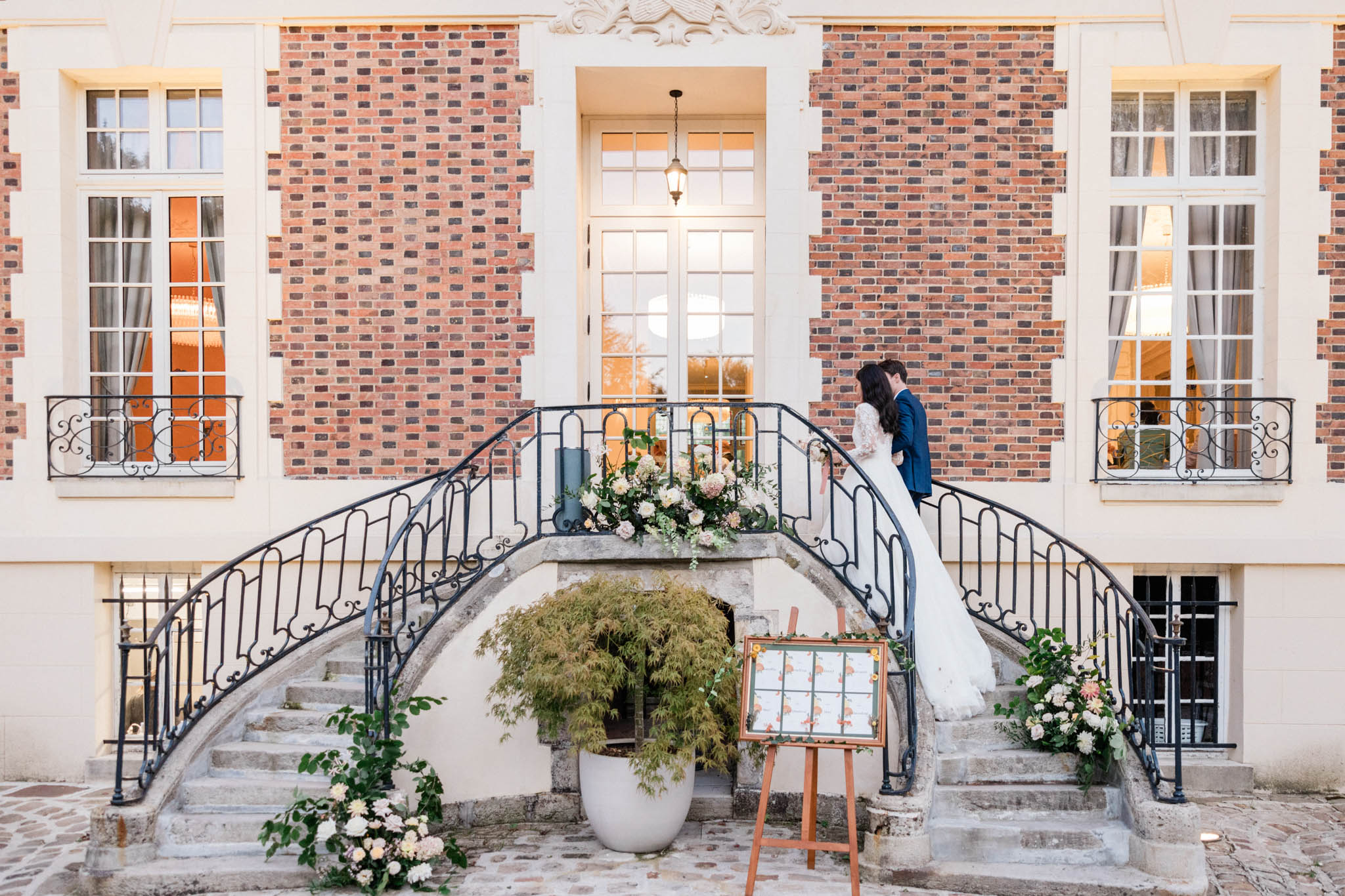 Couple at top of curved staircase with blush dahlia and hydrangea arrangements draped over iron railings