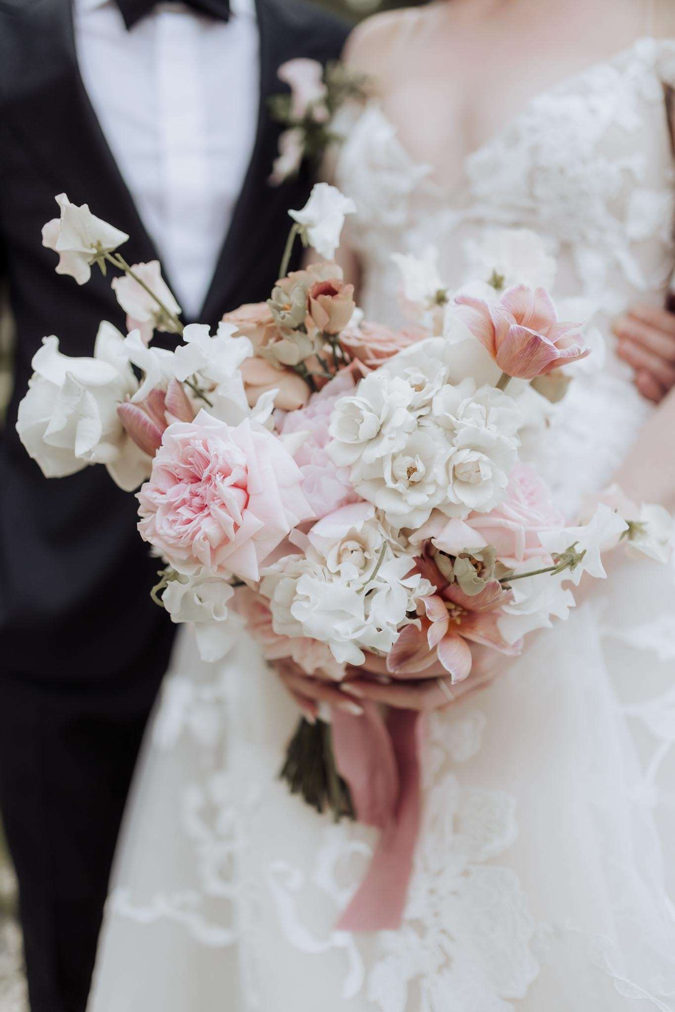 Bride holding a garden-style bouquet of blush roses, white sweet peas, and pink tulips tied with dusty rose ribbon