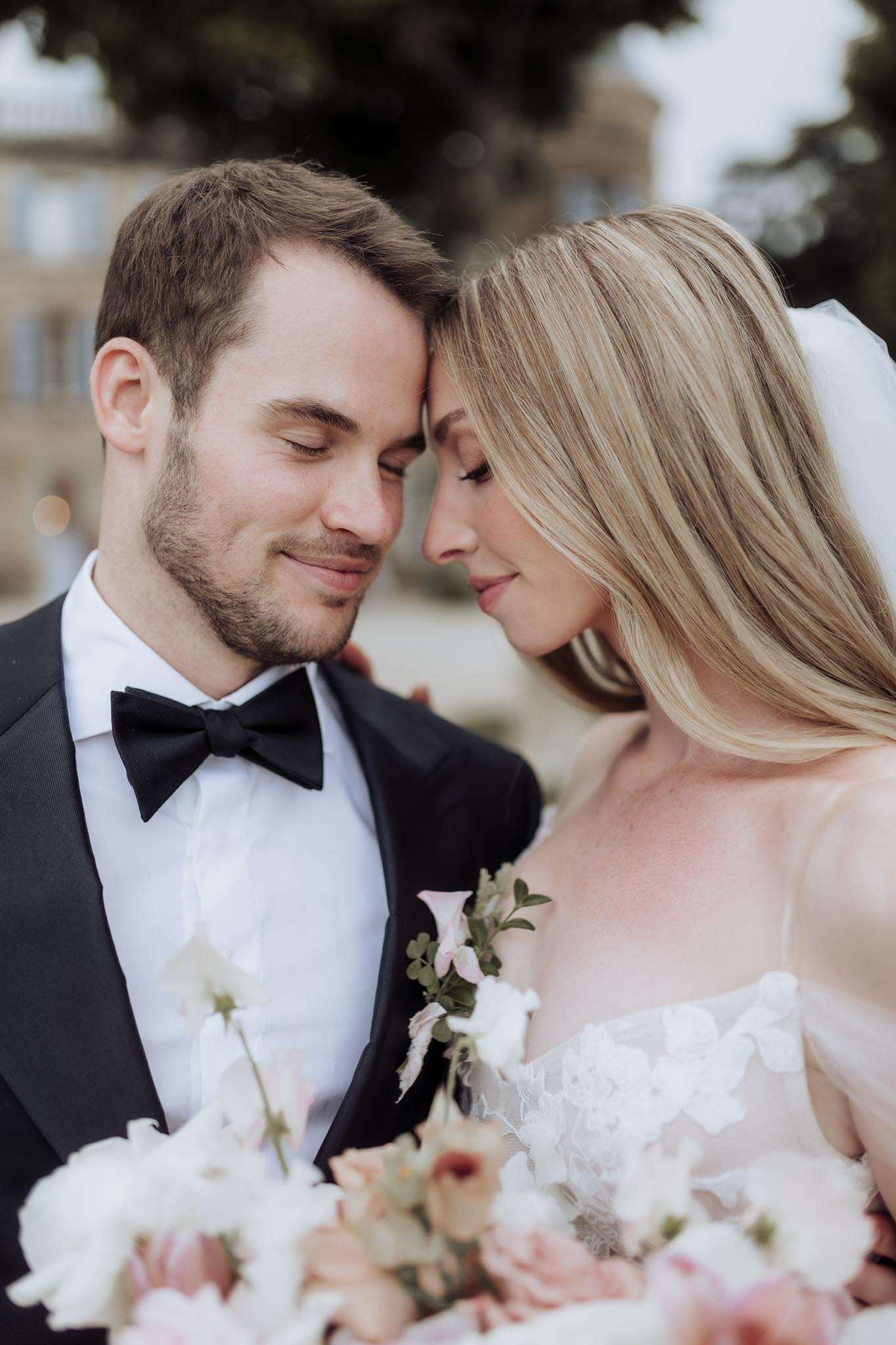 Bride and groom pressing foreheads together with eyes closed, bridal bouquet of white and blush blooms